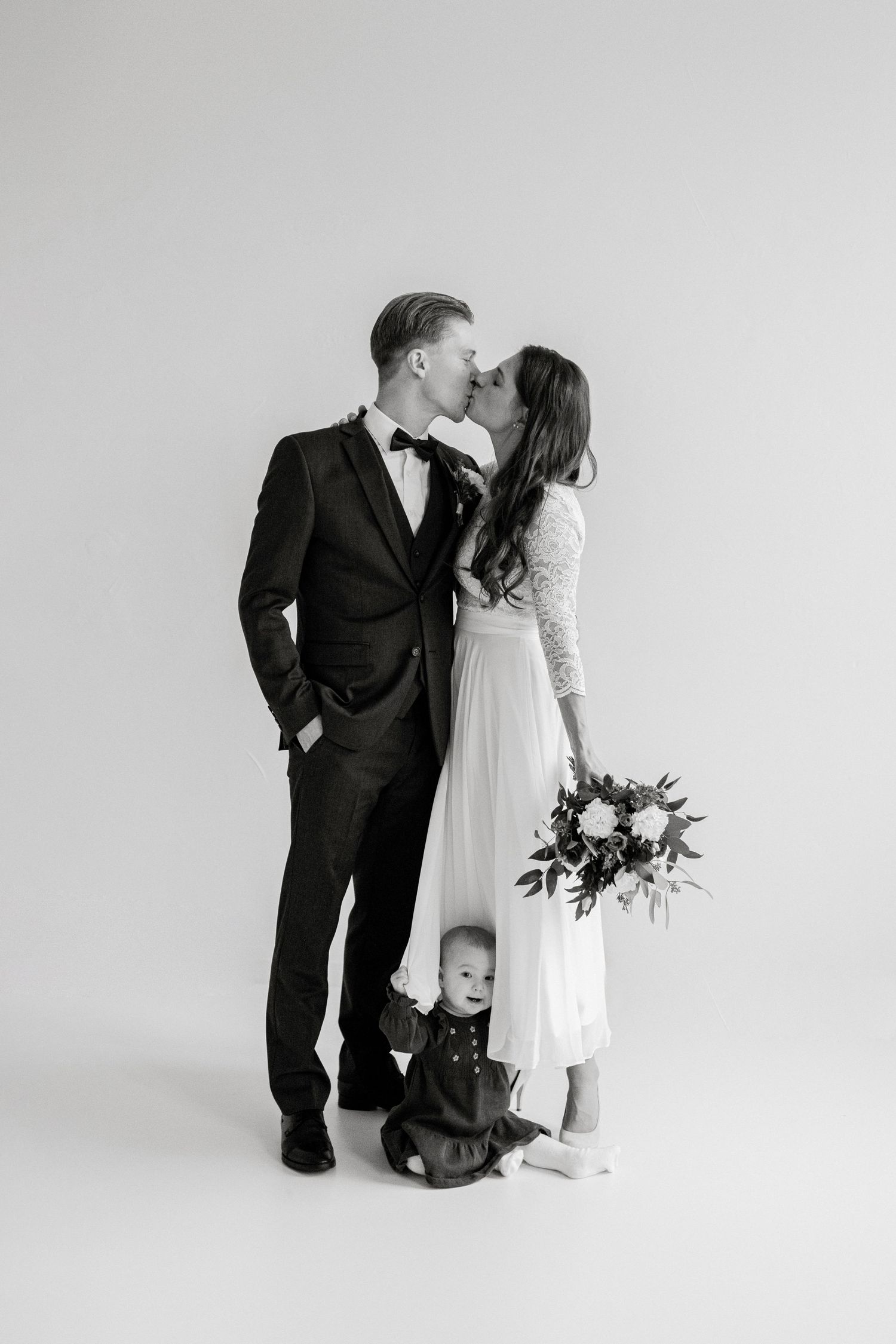 Elegant couple in formal attire sharing romantic moment with small child at their feet.