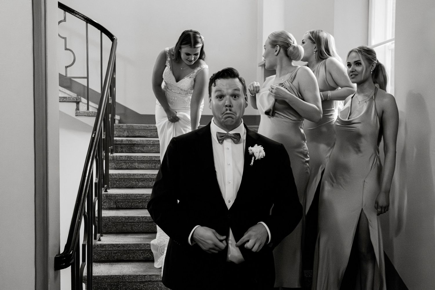 Wedding party members walking down a bright hallway with stairs in formal attire.