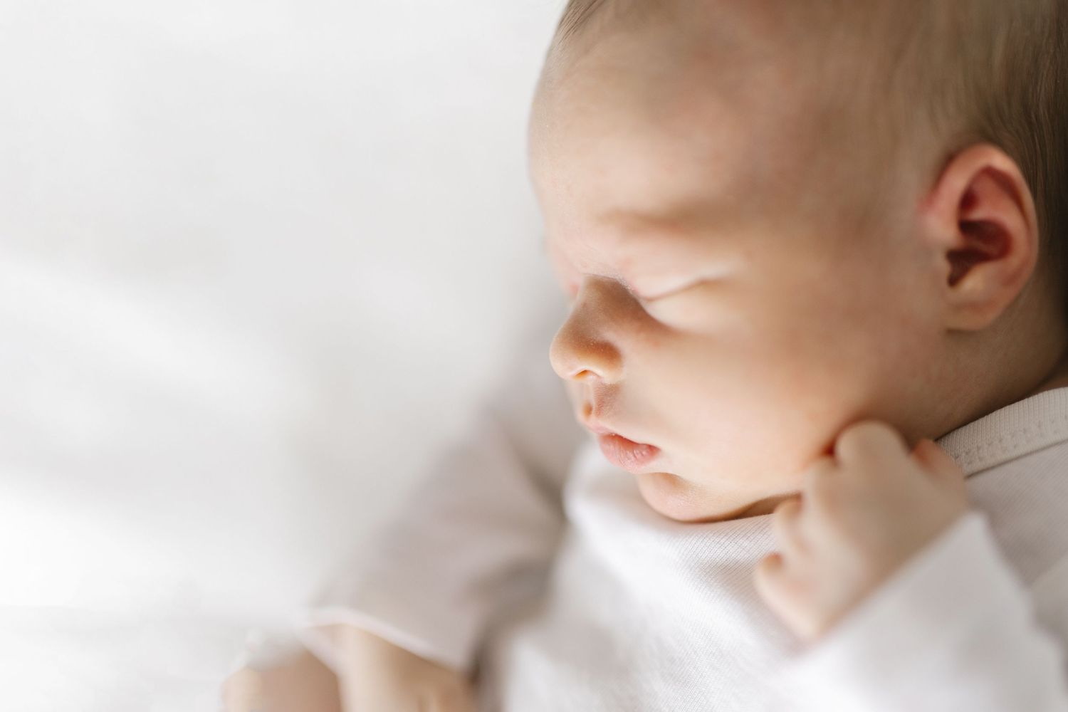 Close-up of a peaceful sleeping newborn baby lying on a soft white blanket in natural light.