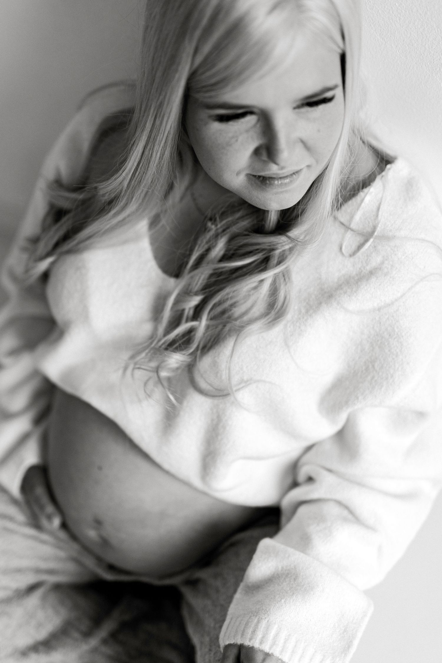 Black and white maternity photo of a blonde woman in a cropped sweater cradling her baby bump.