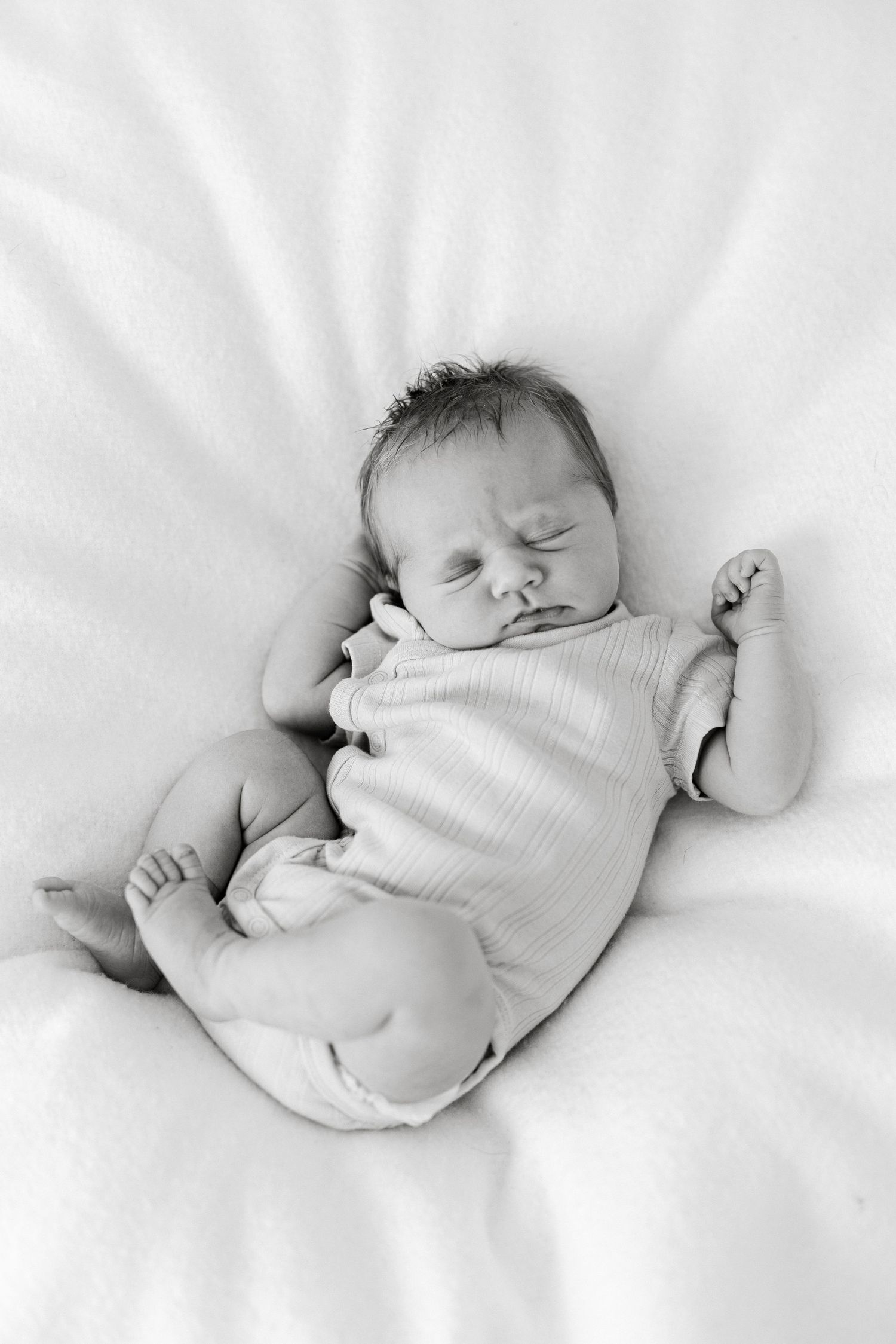 Black and white photo of a peaceful sleeping newborn baby lying on a soft white blanket.