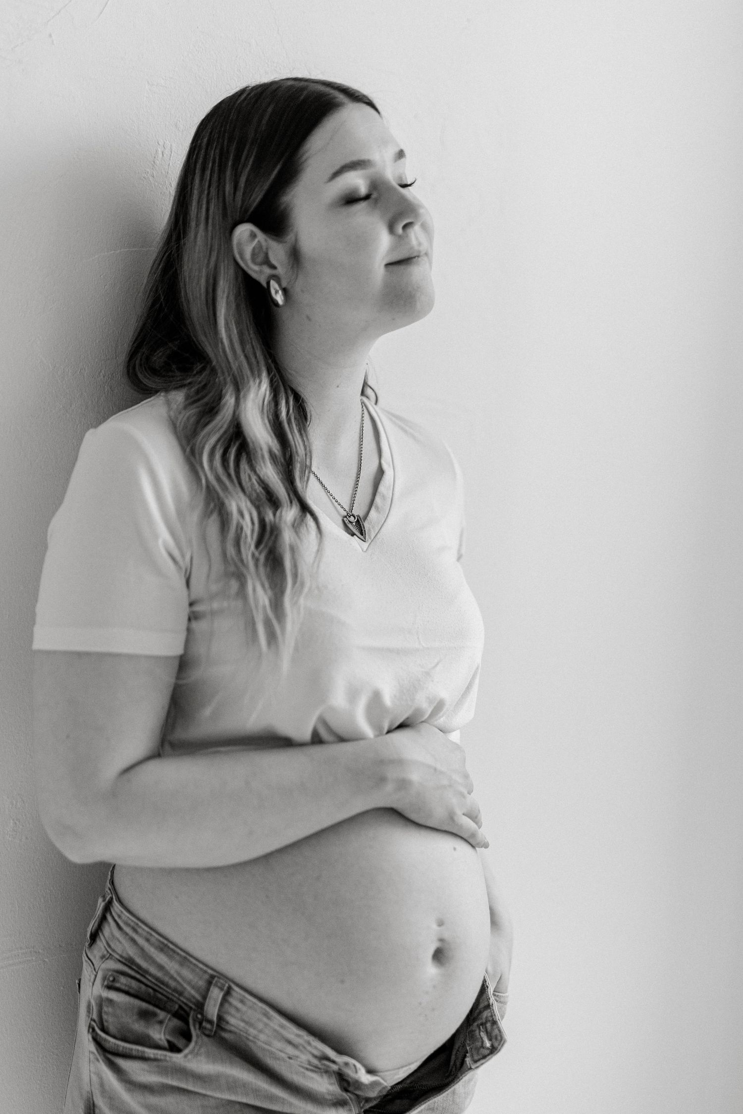 Black and white photo series showing a pregnant person in a white t-shirt and jeans embracing their growing belly.