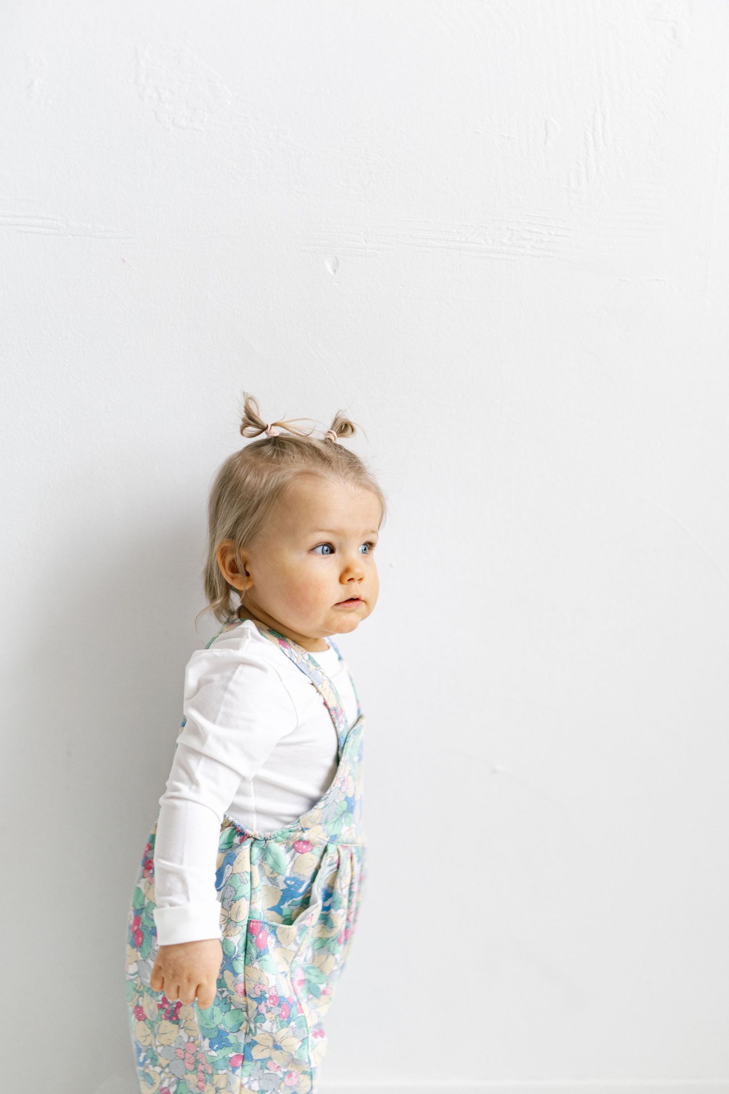 A small child in a white long-sleeve top and floral dress poses against a white background in three sequential photos.