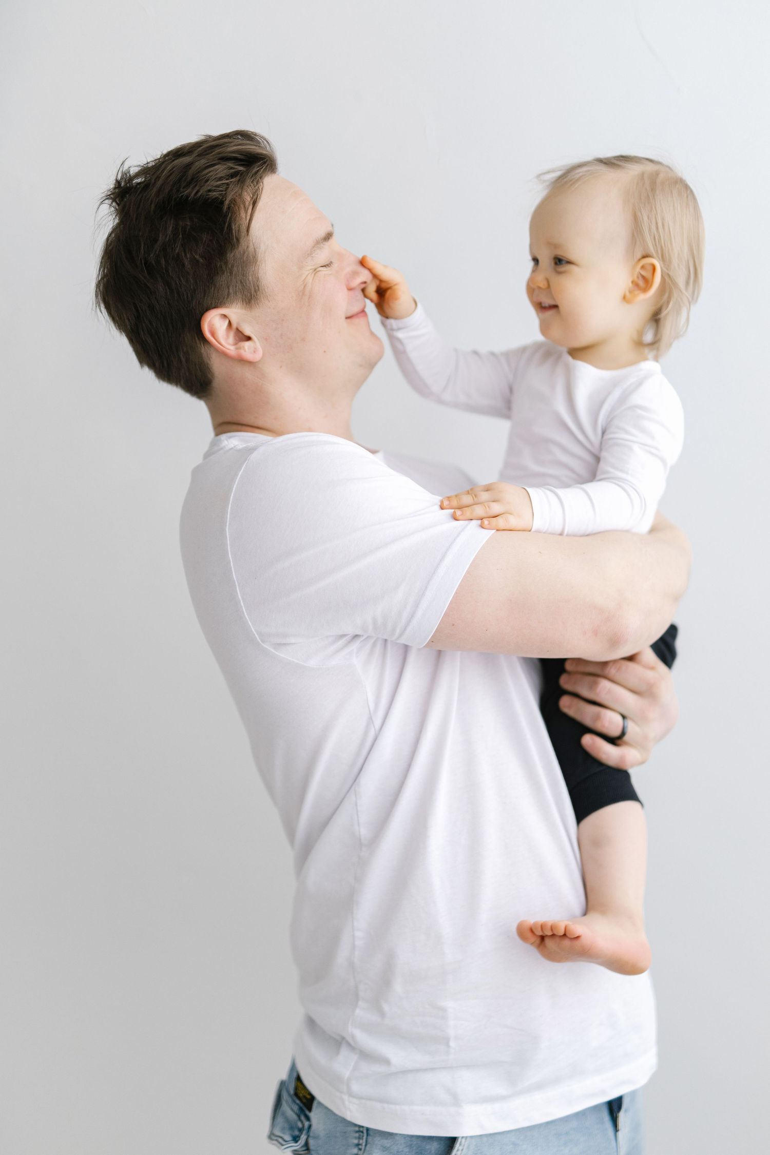 A playful moment between parent and toddler in white shirts against a light background.