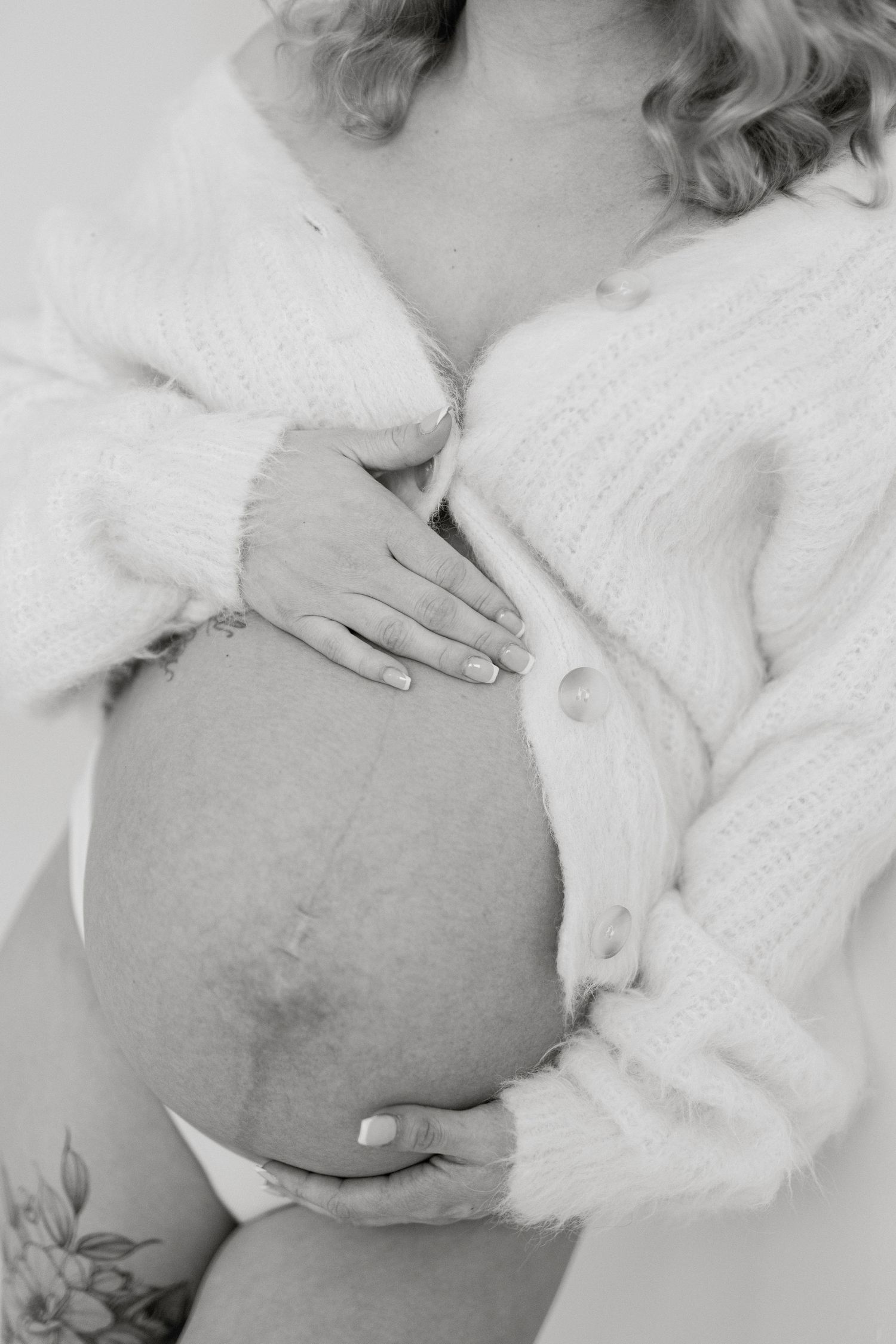 Close-up black and white photo of hands cradling pregnant belly in cozy sweater.
