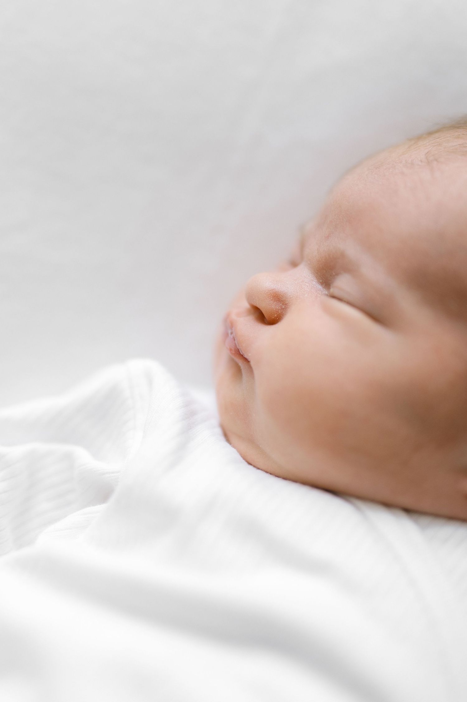 Close-up profile of sleeping newborn against white bedding.