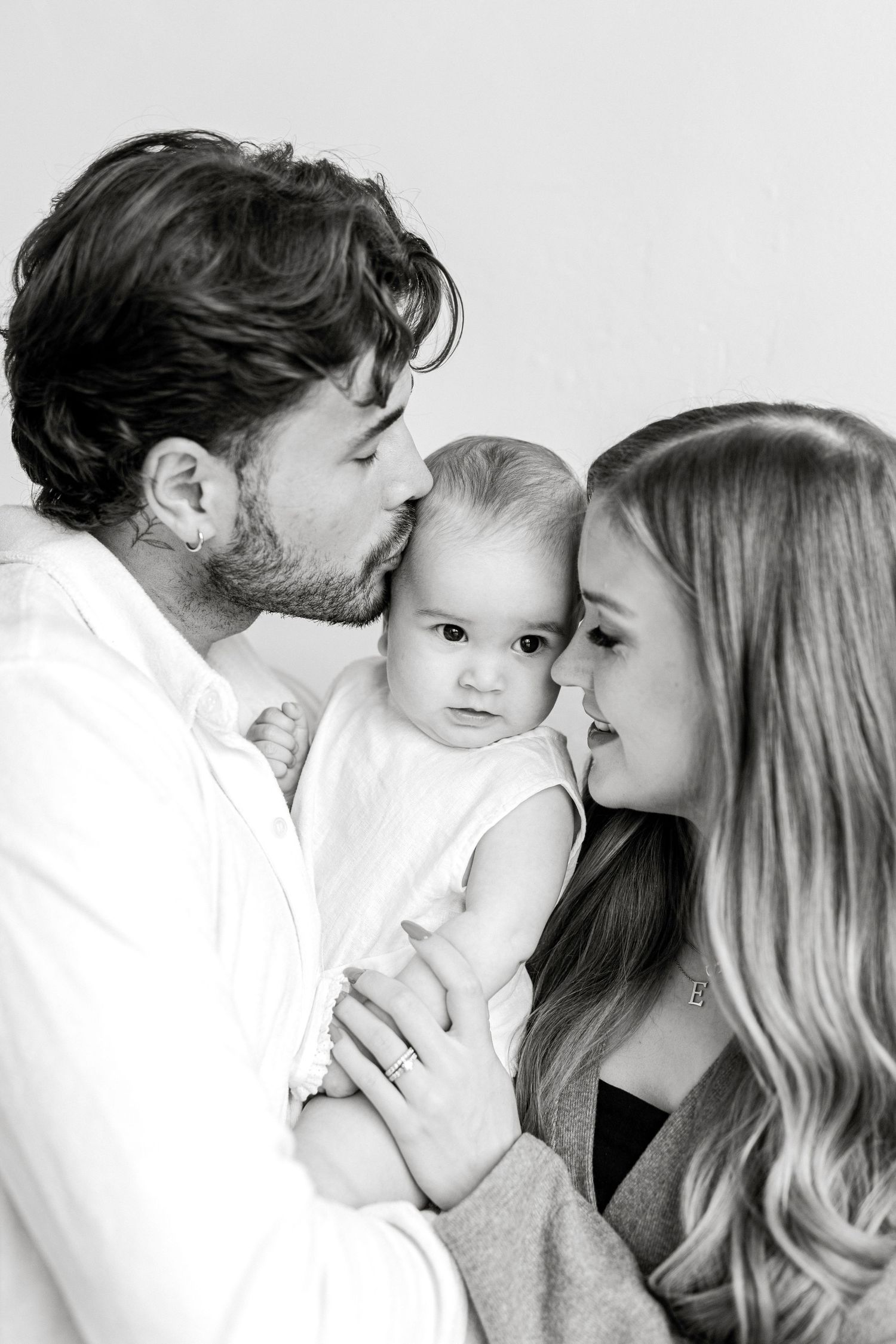 Black and white photo of parents kissing their baby, a tender family portrait moment.