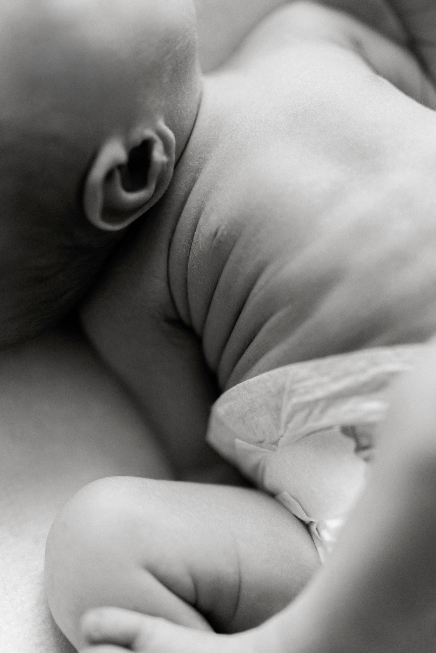 Black and white close-up photo of a sleeping newborn baby with tiny fingers and soft skin folds.