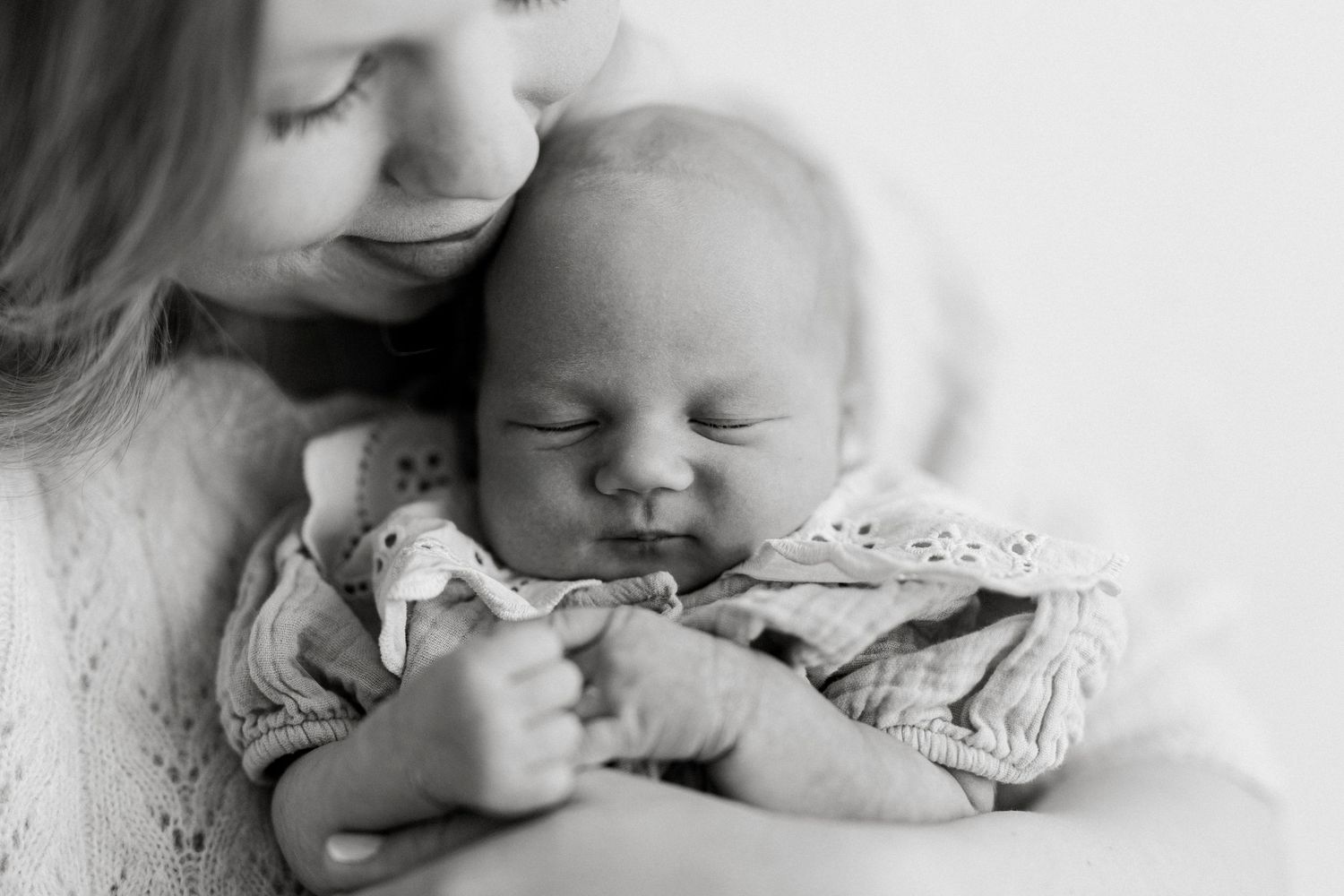 Black and white photo of a mother tenderly holding her sleeping newborn baby close to her face.