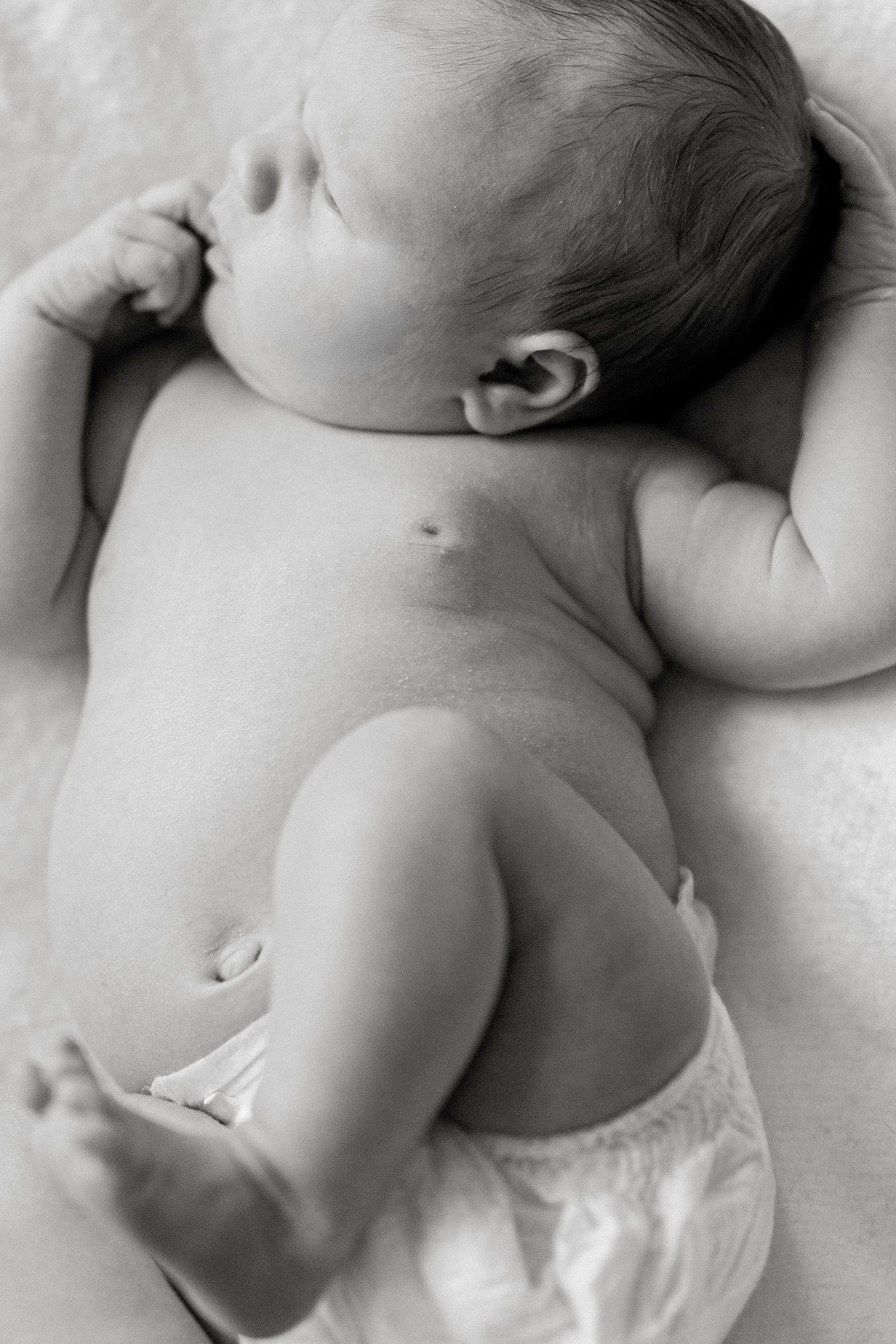Black and white photo of a peaceful newborn baby lying on its back wearing a diaper.