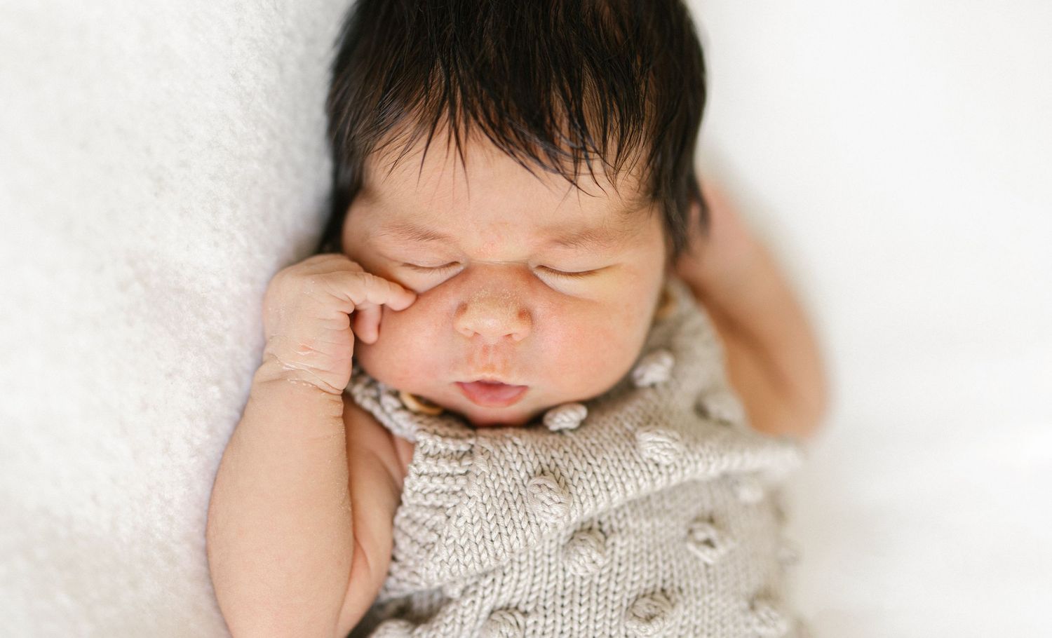 Peaceful newborn baby sleeping in a cozy knit outfit on a soft white blanket.