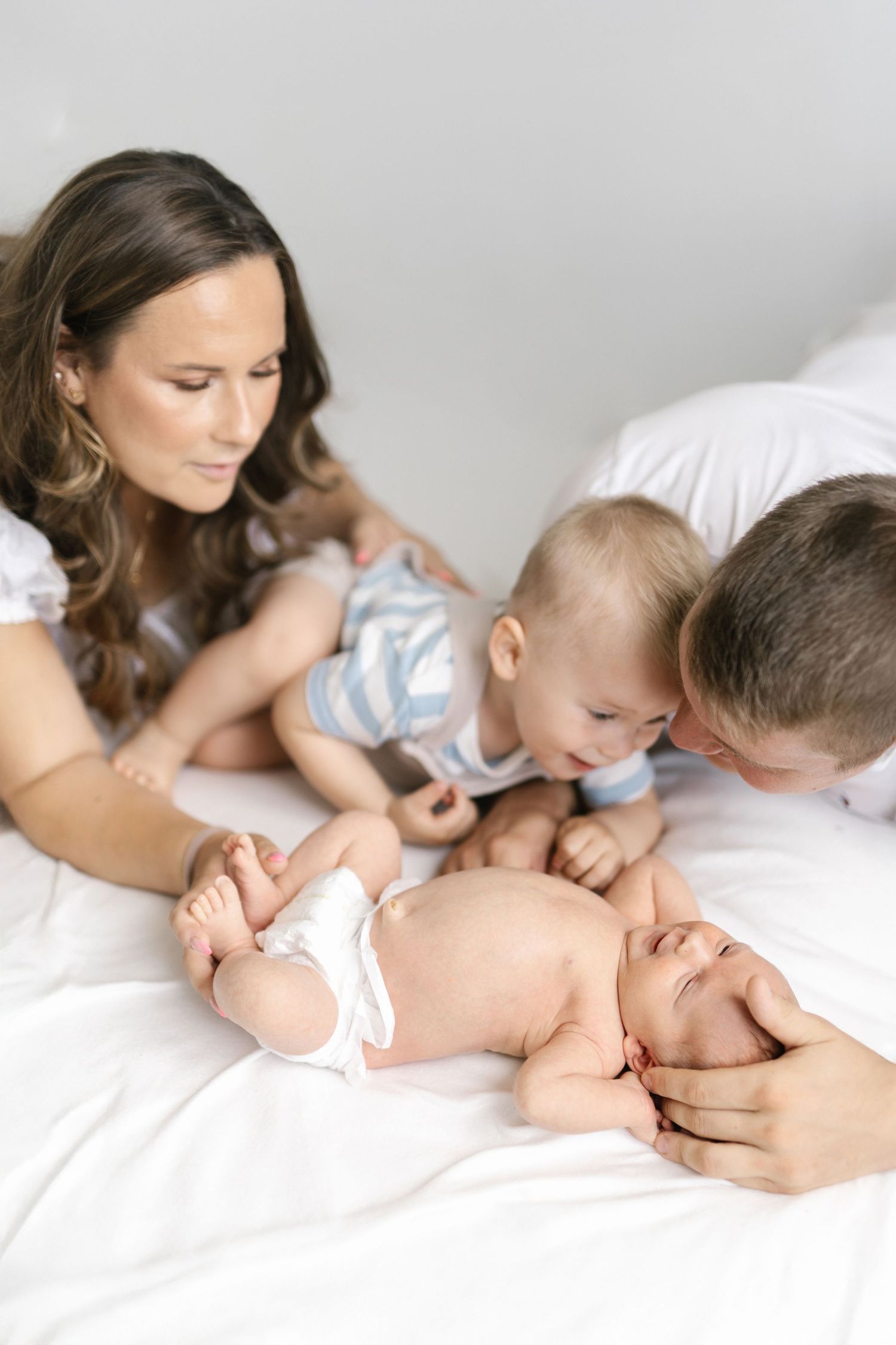 Family gathered on white bedding admiring their newborn baby together in a tender moment.