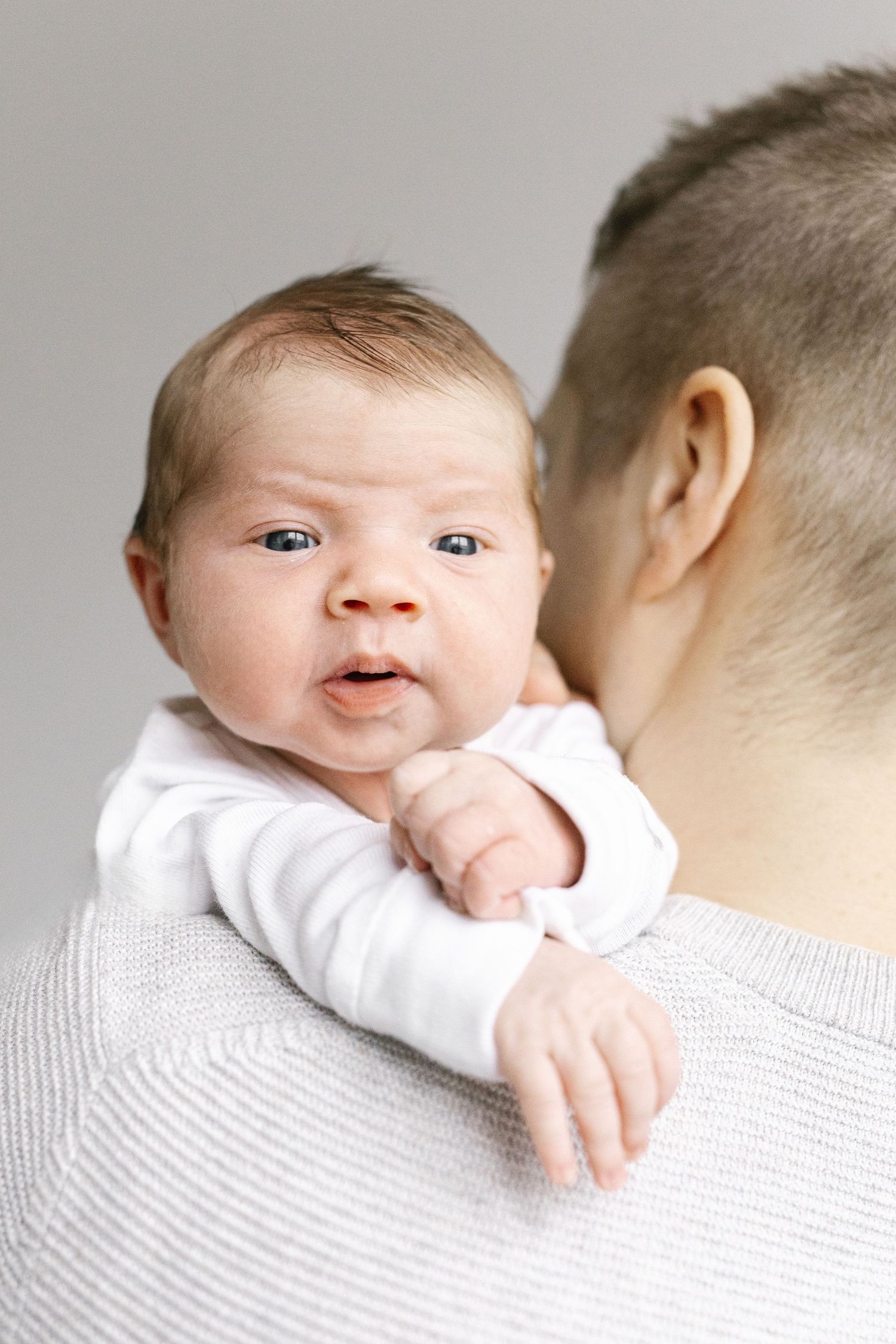 Baby peering over parent's shoulder in white clothing.