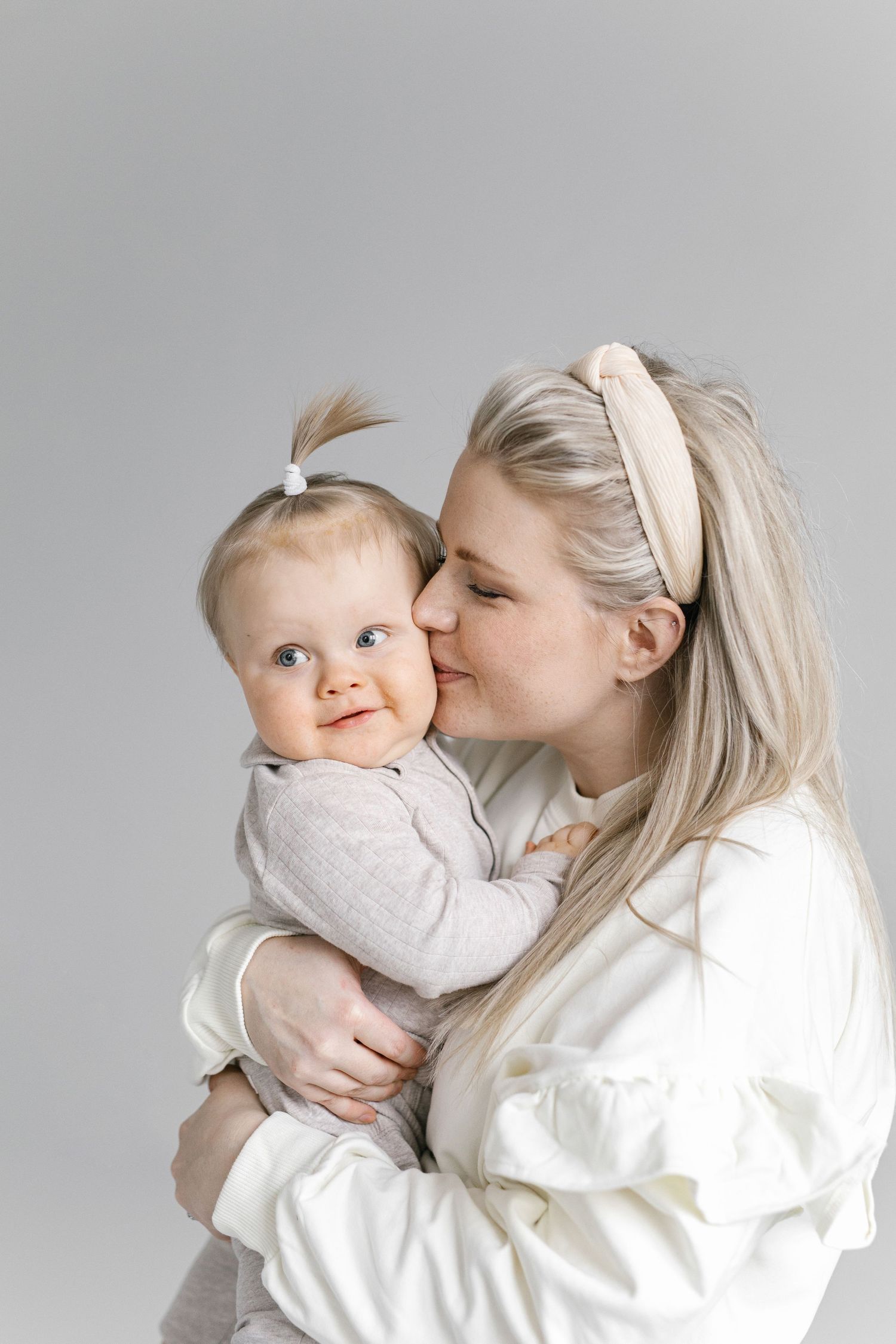A tender moment captured as a woman in white kisses a baby in gray.