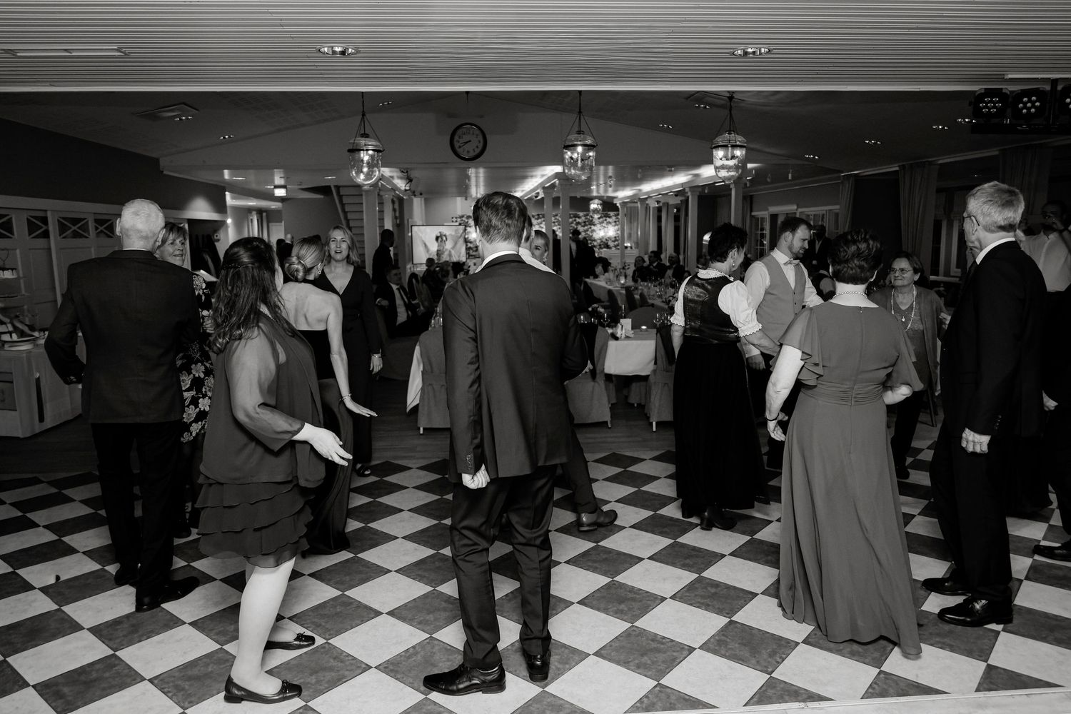 Guests dance on classic black and white checkered floor at elegant wedding reception in black and white.