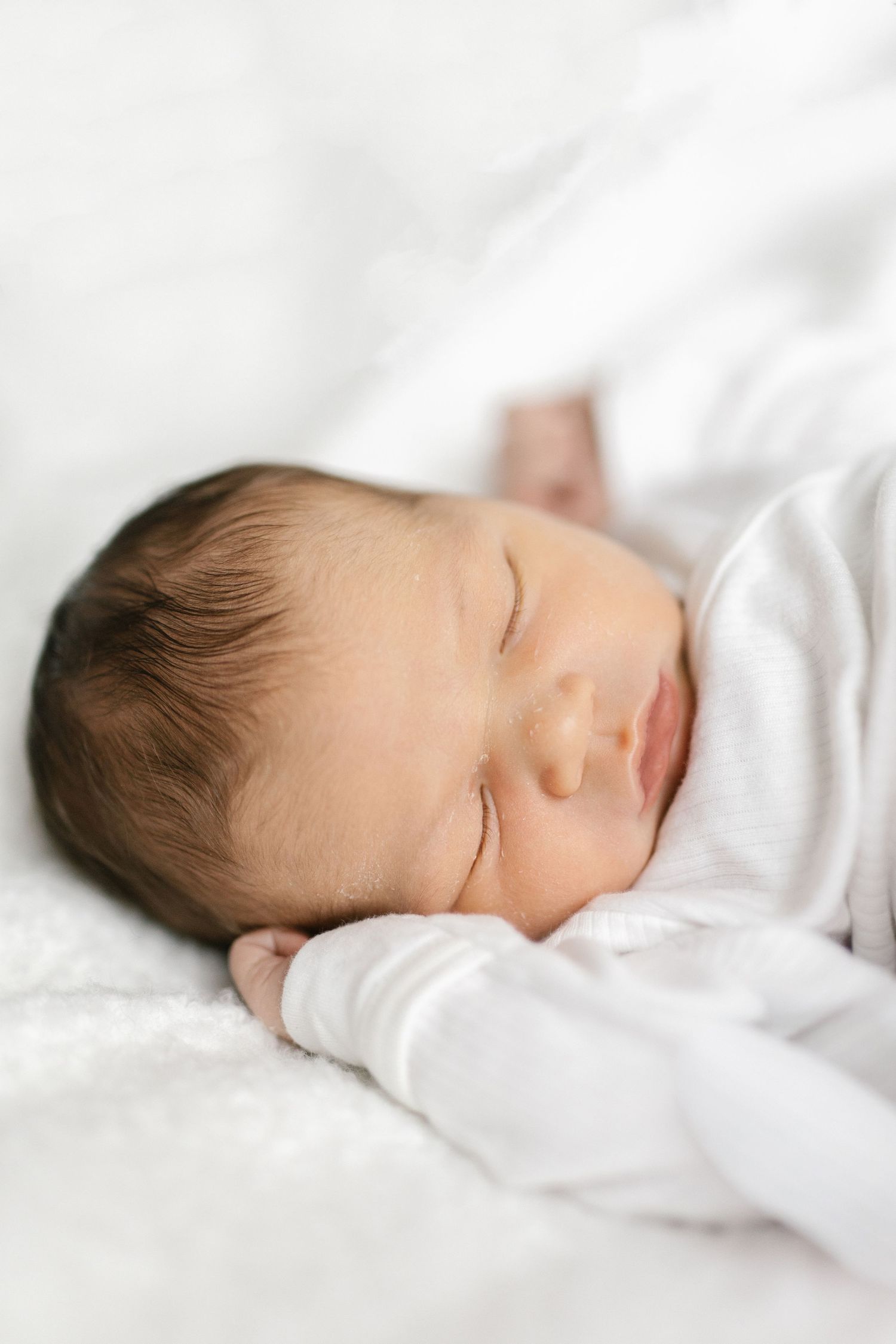 Peaceful sleeping newborn in white clothing against white bedding.