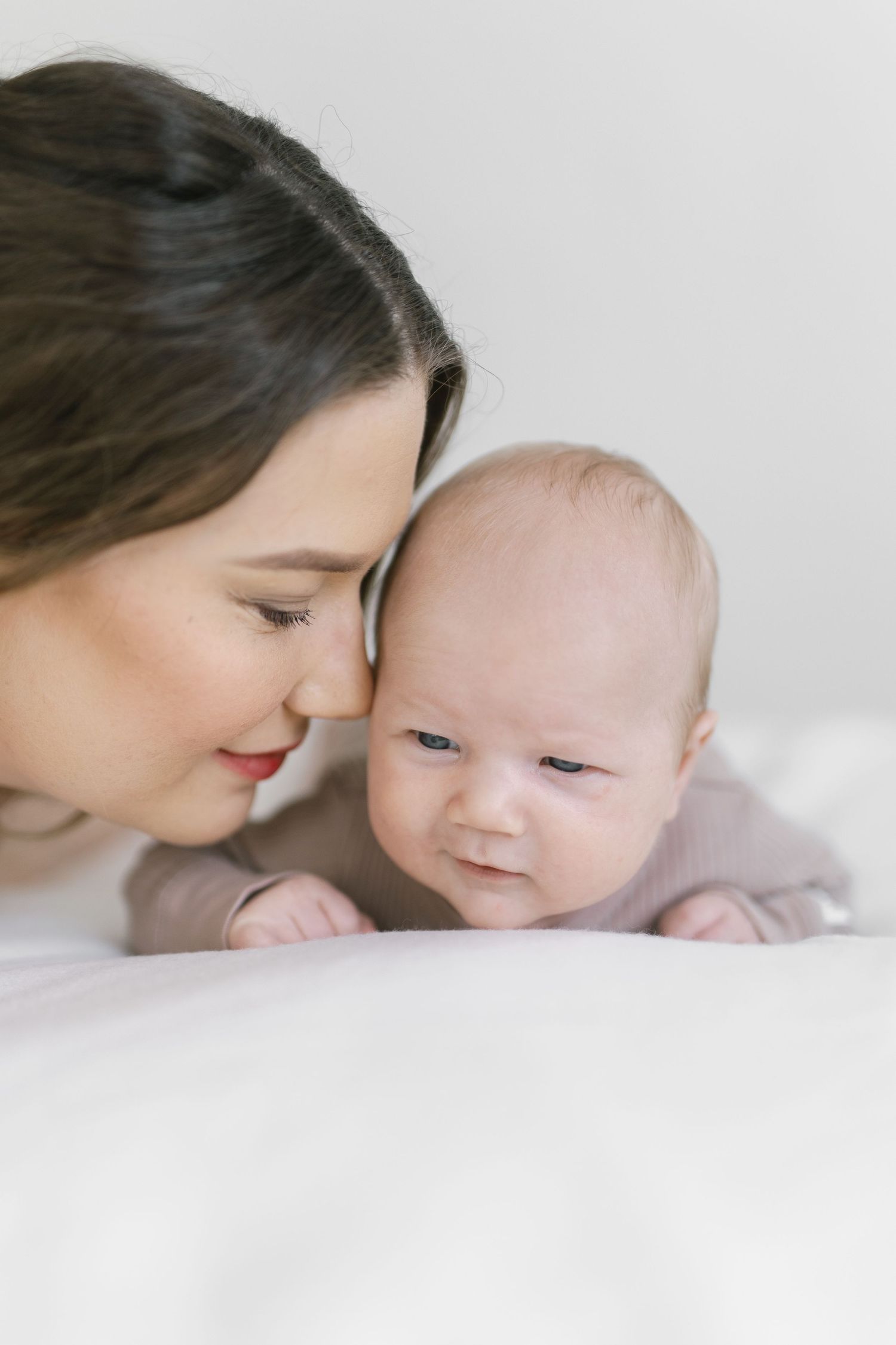 A tender moment as a dark-haired mother gazes lovingly at her newborn baby lying on a white bed.