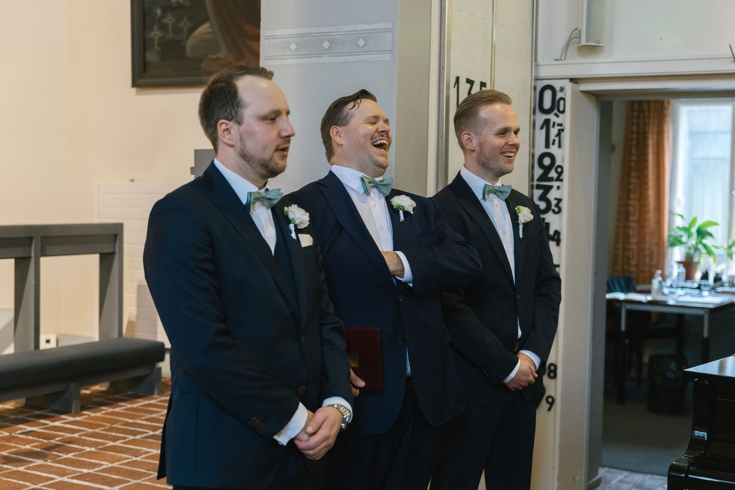Three groomsmen laughing together during wedding ceremony.