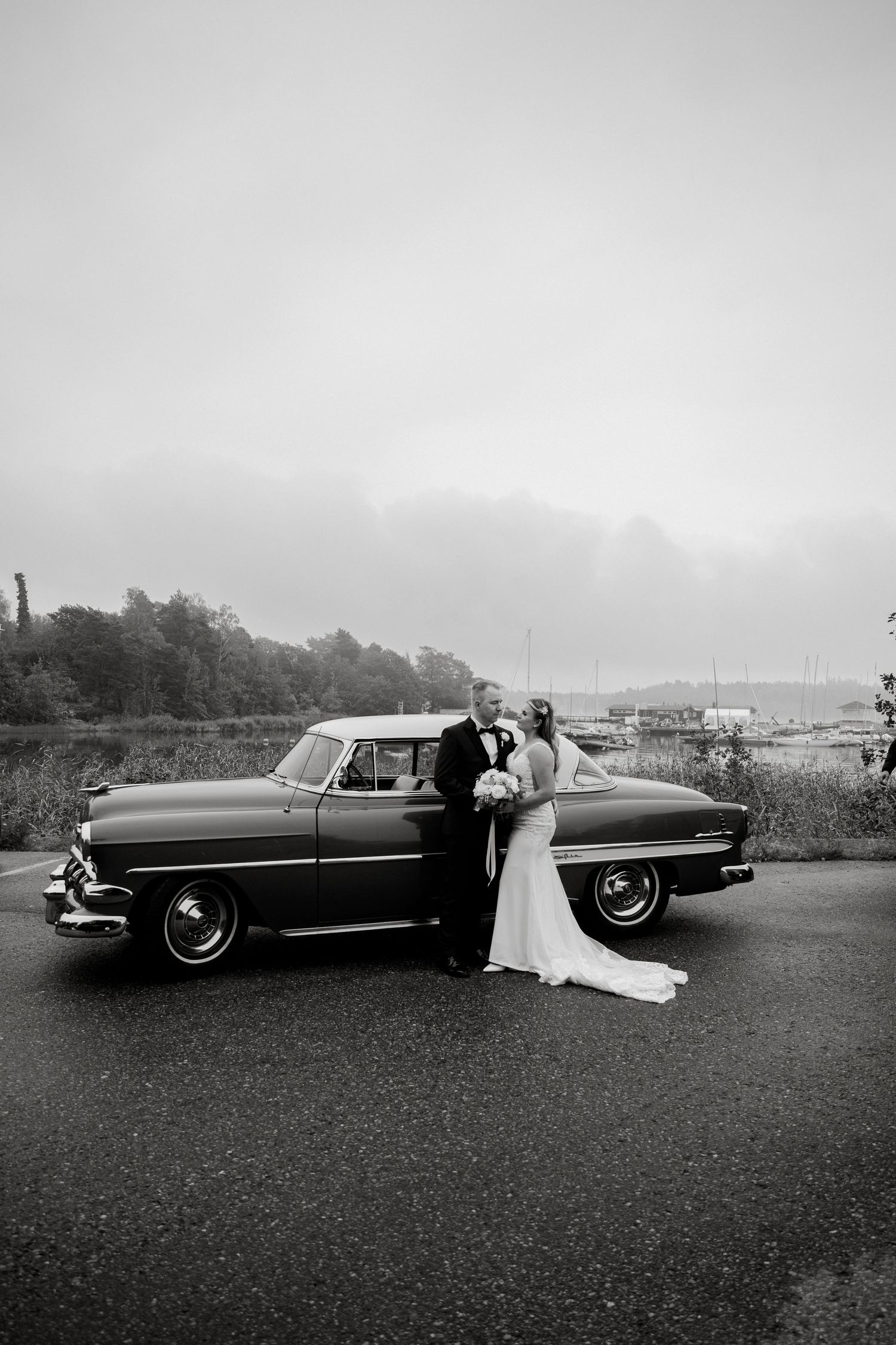 A classic vintage car serves as backdrop for an elegant black and white wedding photo.