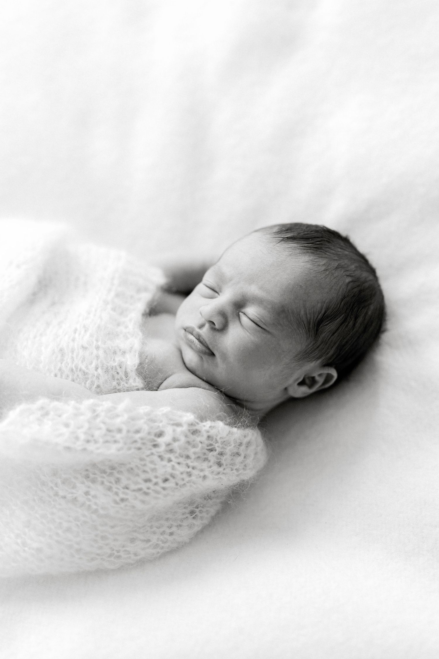 Black and white photo of a peaceful sleeping newborn baby swaddled in a soft white knit wrap.
