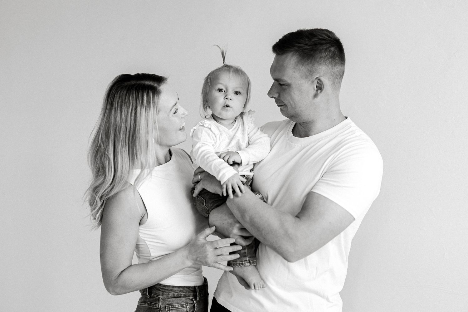 Black and white family portrait of parents lovingly holding their baby in a bright studio setting.