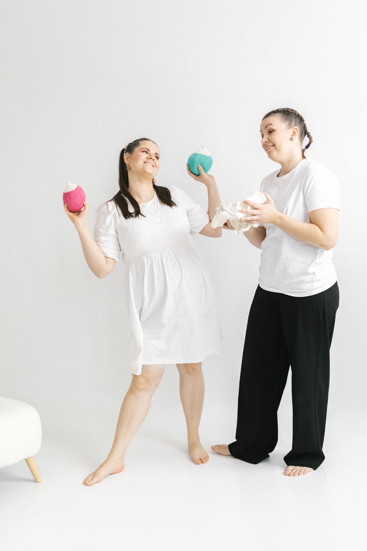 Two smiling women in white tops hold colorful knitted balls against a white background.
