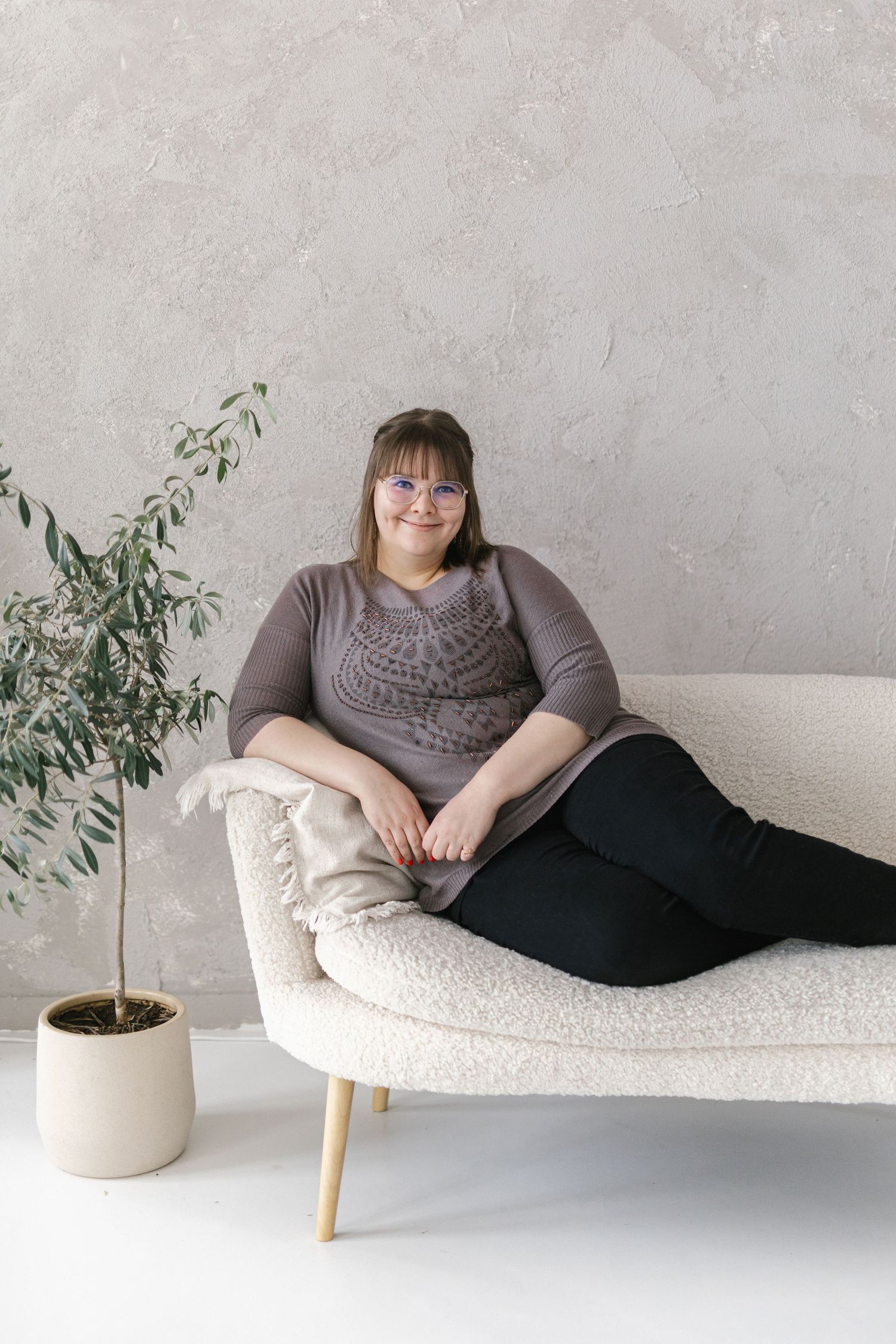 Person in gray sweater relaxing on white modern sofa with potted plant in minimalist interior setting.