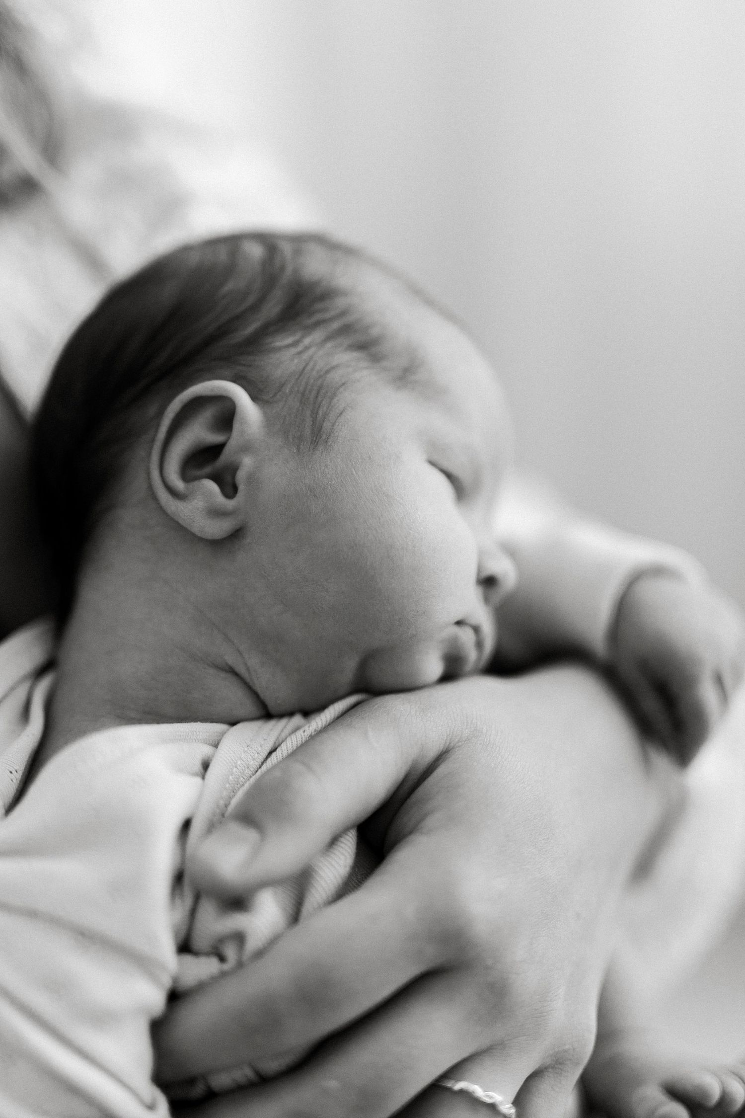 Black and white photo of a sleeping newborn baby cradled gently in a parent's arms.