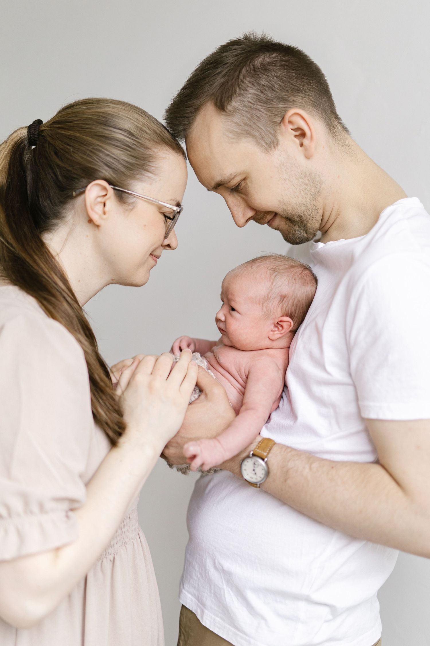 New parents tenderly holding their newborn baby together, sharing an intimate forehead-to-forehead moment in a studio.