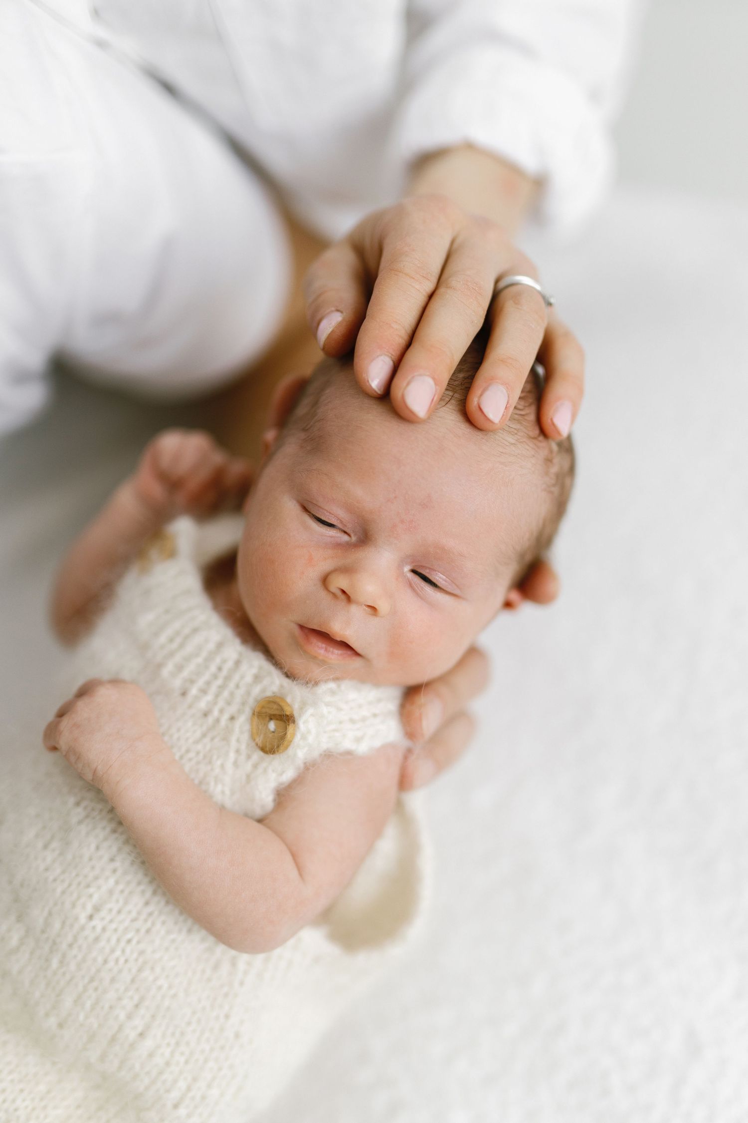Peaceful sleeping newborn wrapped in white knit fabric during professional photo session.