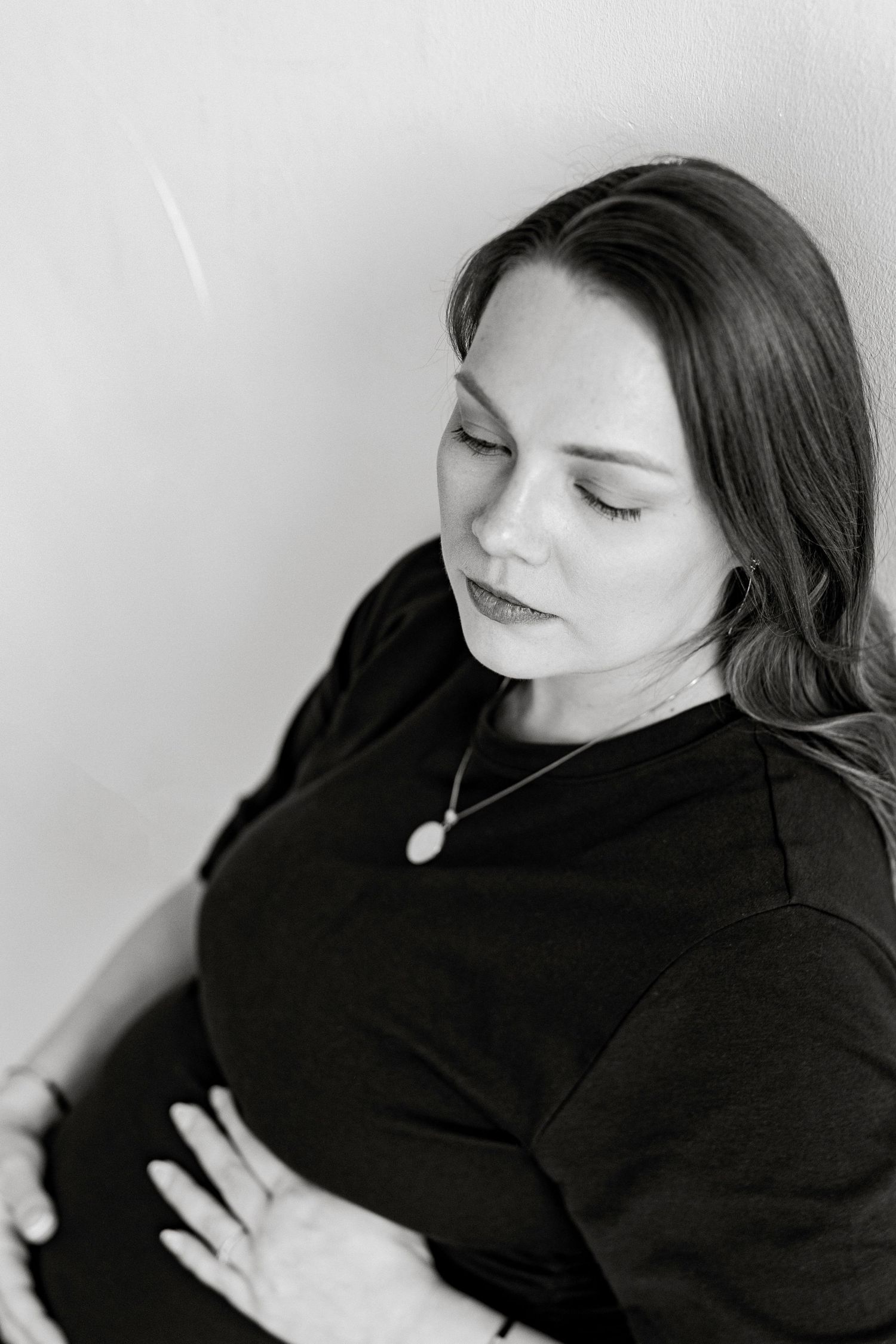 Black and white maternity photo of a woman in a black dress cradling her baby bump, looking down peacefully.