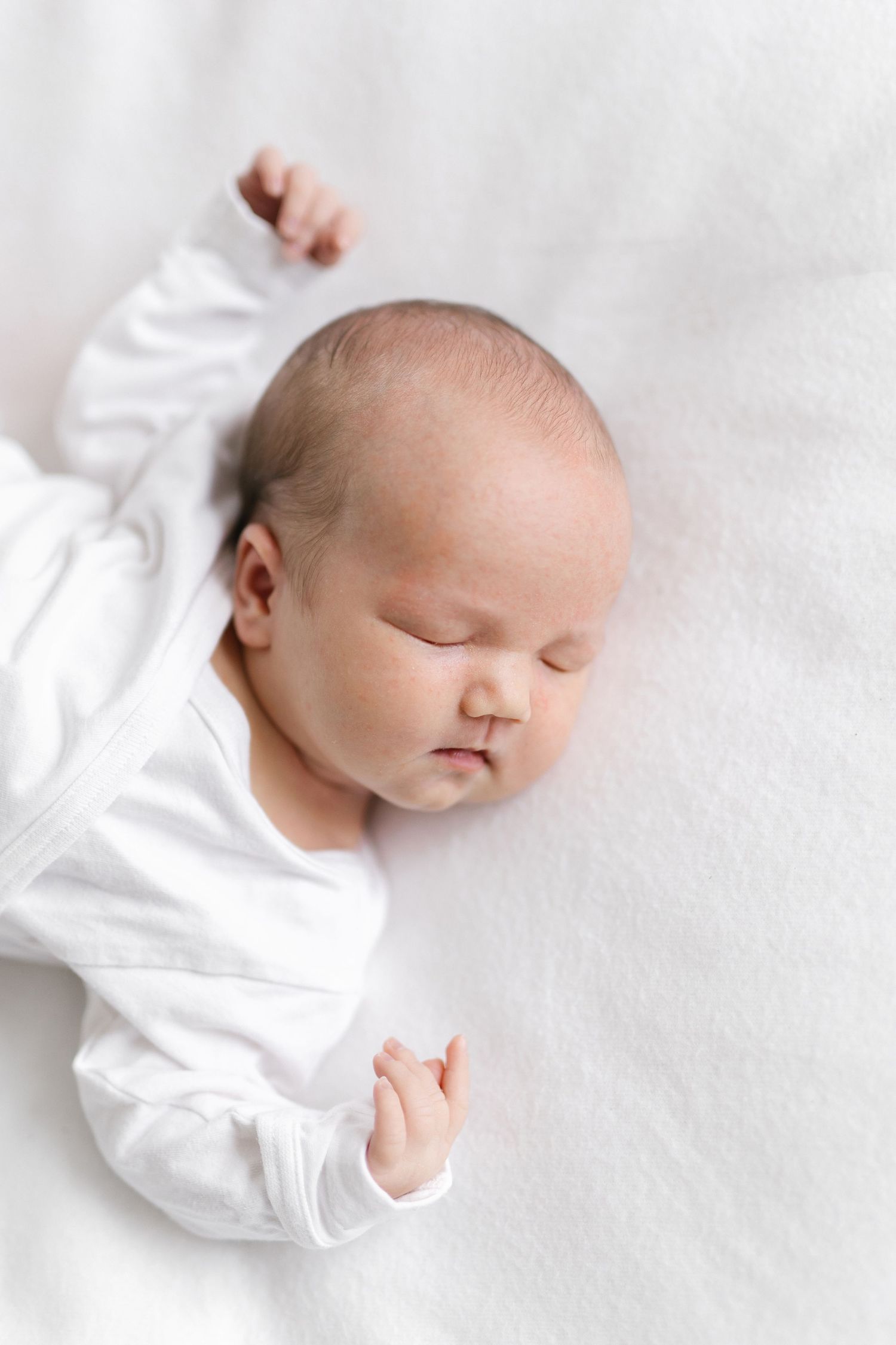 Peaceful newborn baby sleeping on soft white bedding in minimalist photography style.