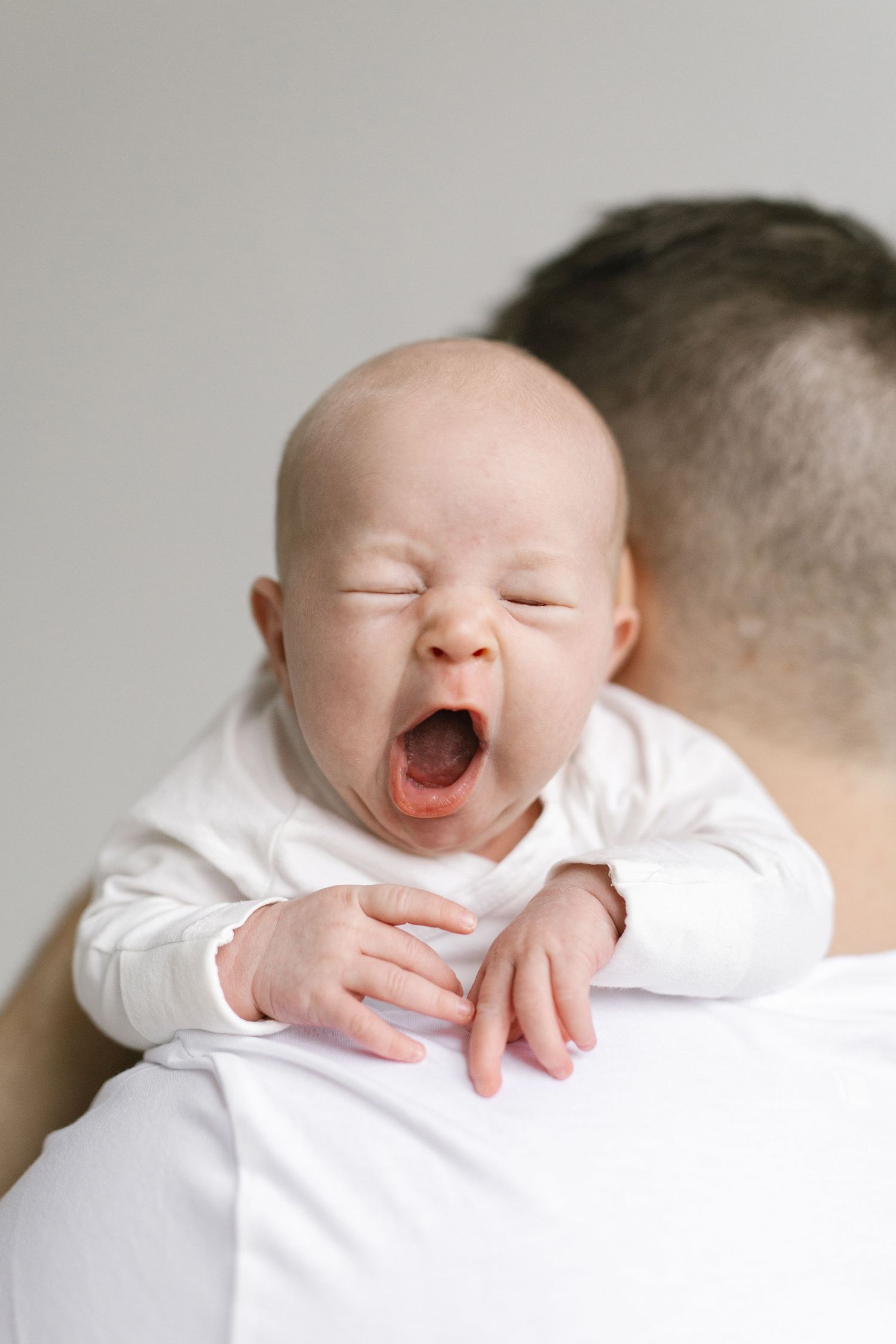 Baby in white clothing laughing while being held over shoulder in sequence.