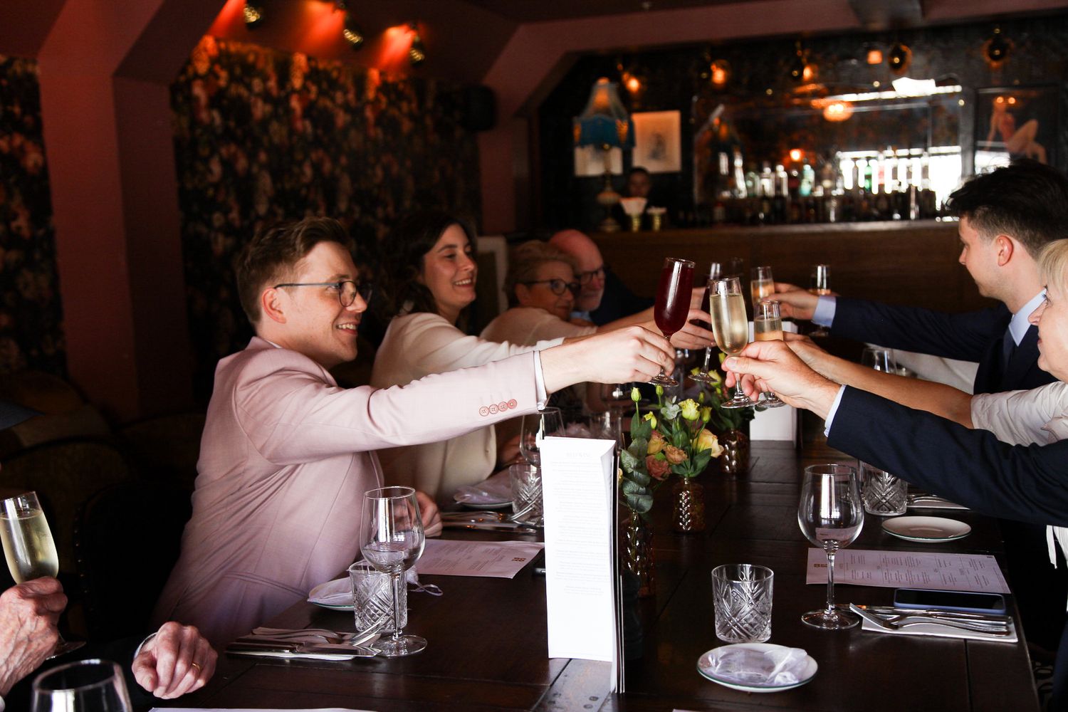 People toasting with red wine glasses at a restaurant dinner table in a dimly lit dining room.
