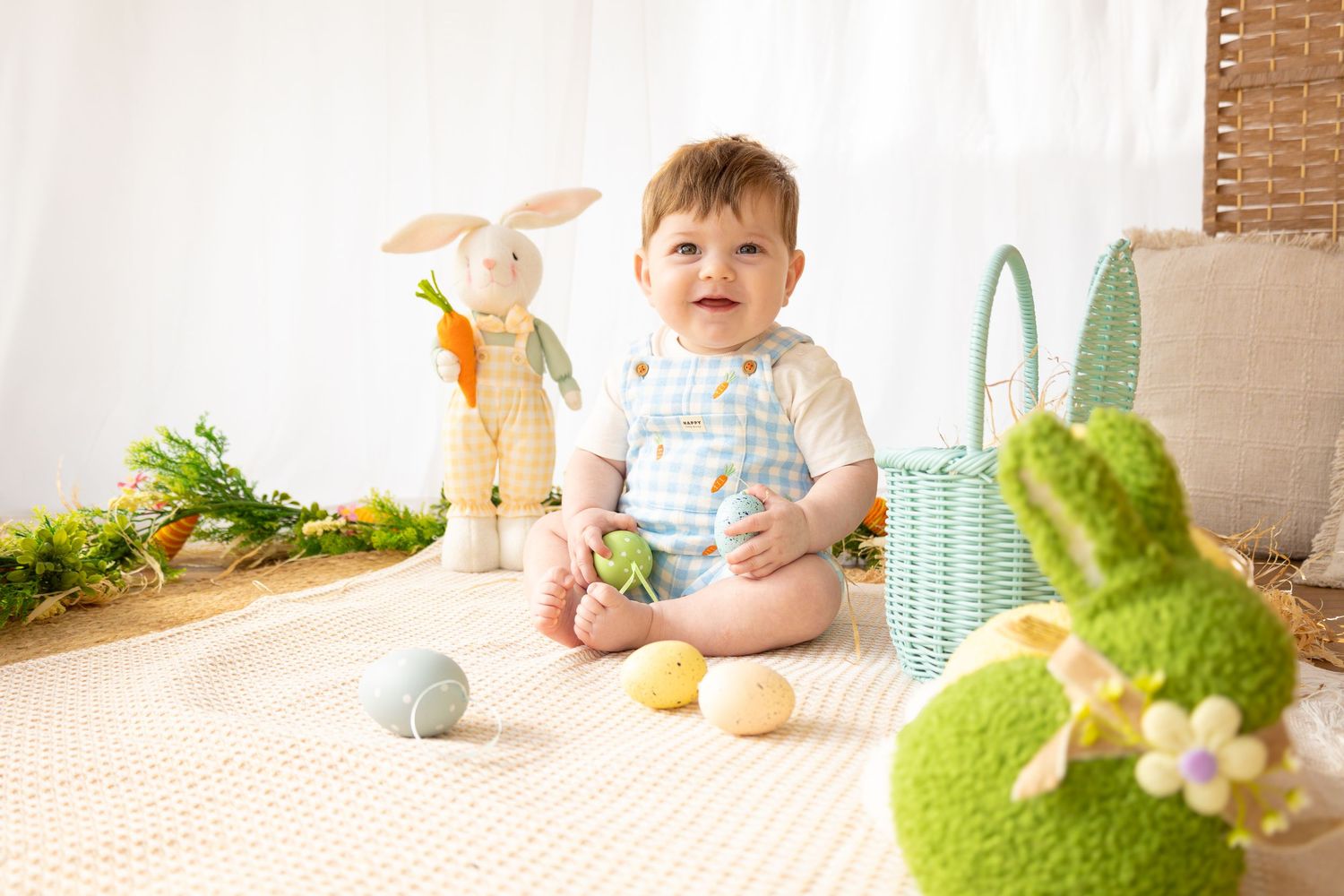 Baby sitting among Easter eggs, plush bunny toys, and a green basket in a bright, festive holiday photo setup.