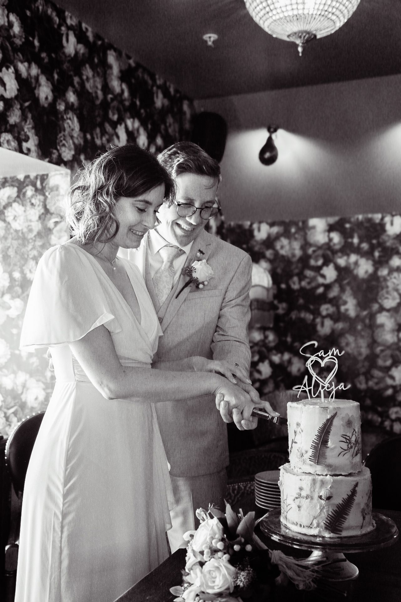 Wedding couple cutting their elegant white cake under a crystal chandelier.