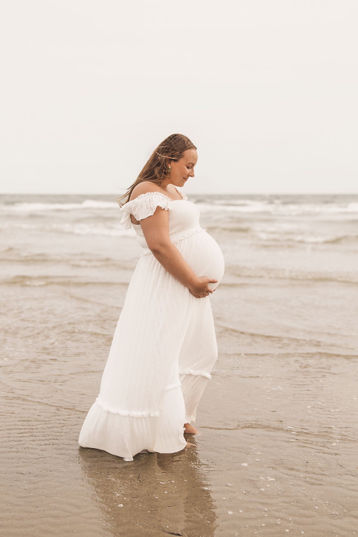 Woman in white dress plays joyfully in ocean waves at beach.