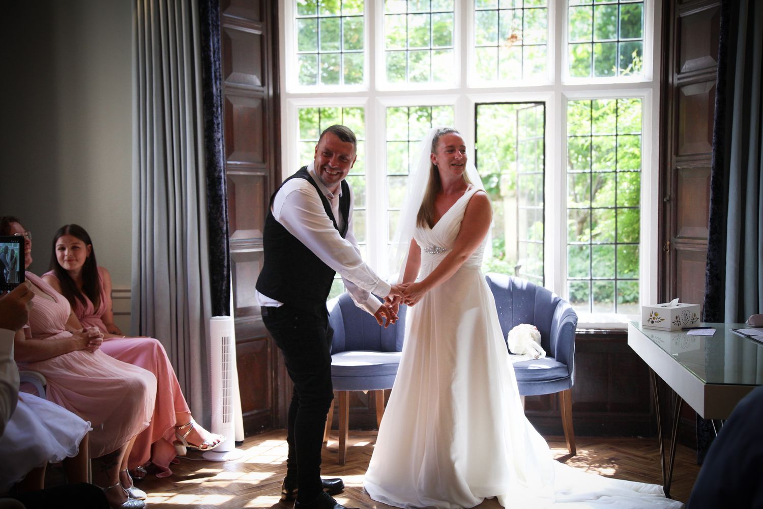 A couple shares a tender moment during their wedding ceremony by a bright window in an elegant room.