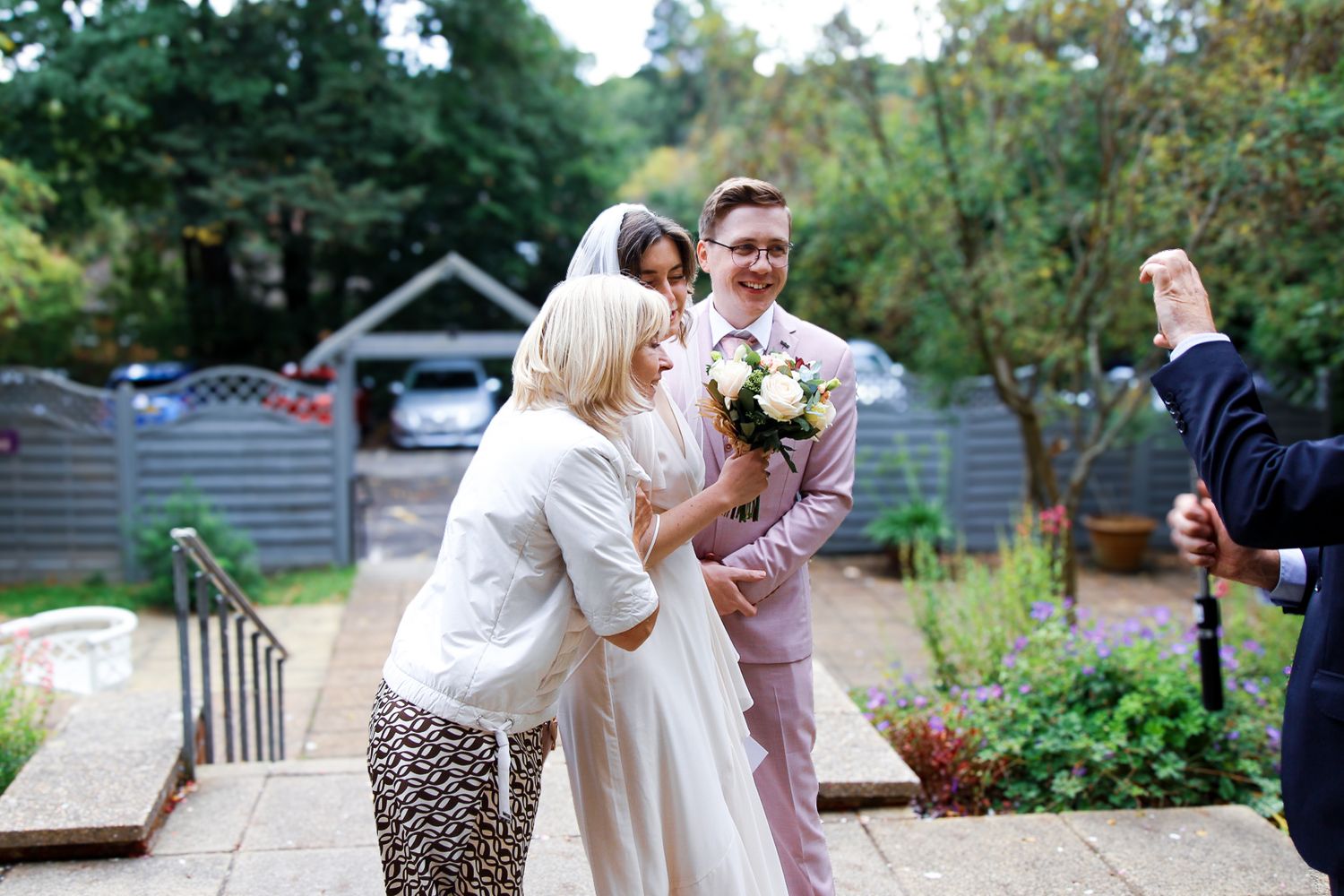 Wedding party celebrating outdoors in garden setting with greenery.