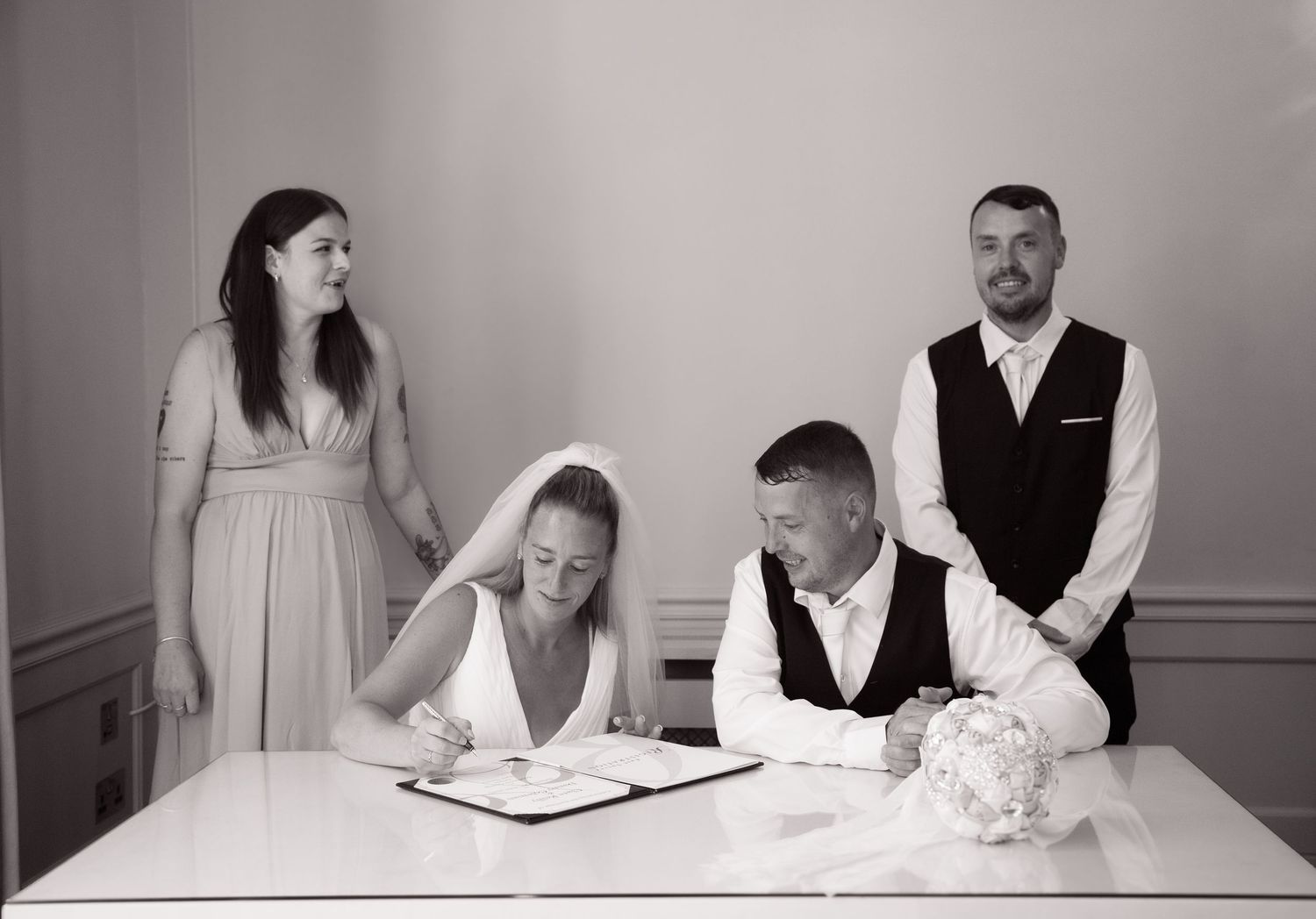 A formal document signing ceremony with attendants gathered around a white table.