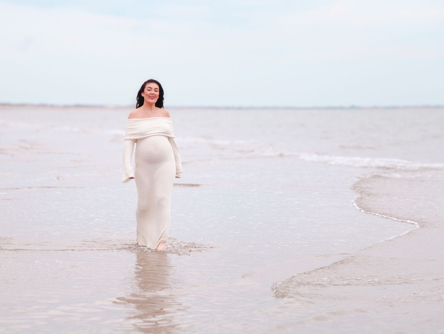 Ethereal beach photoshoot featuring flowing white dress against soft coastal backdrop.