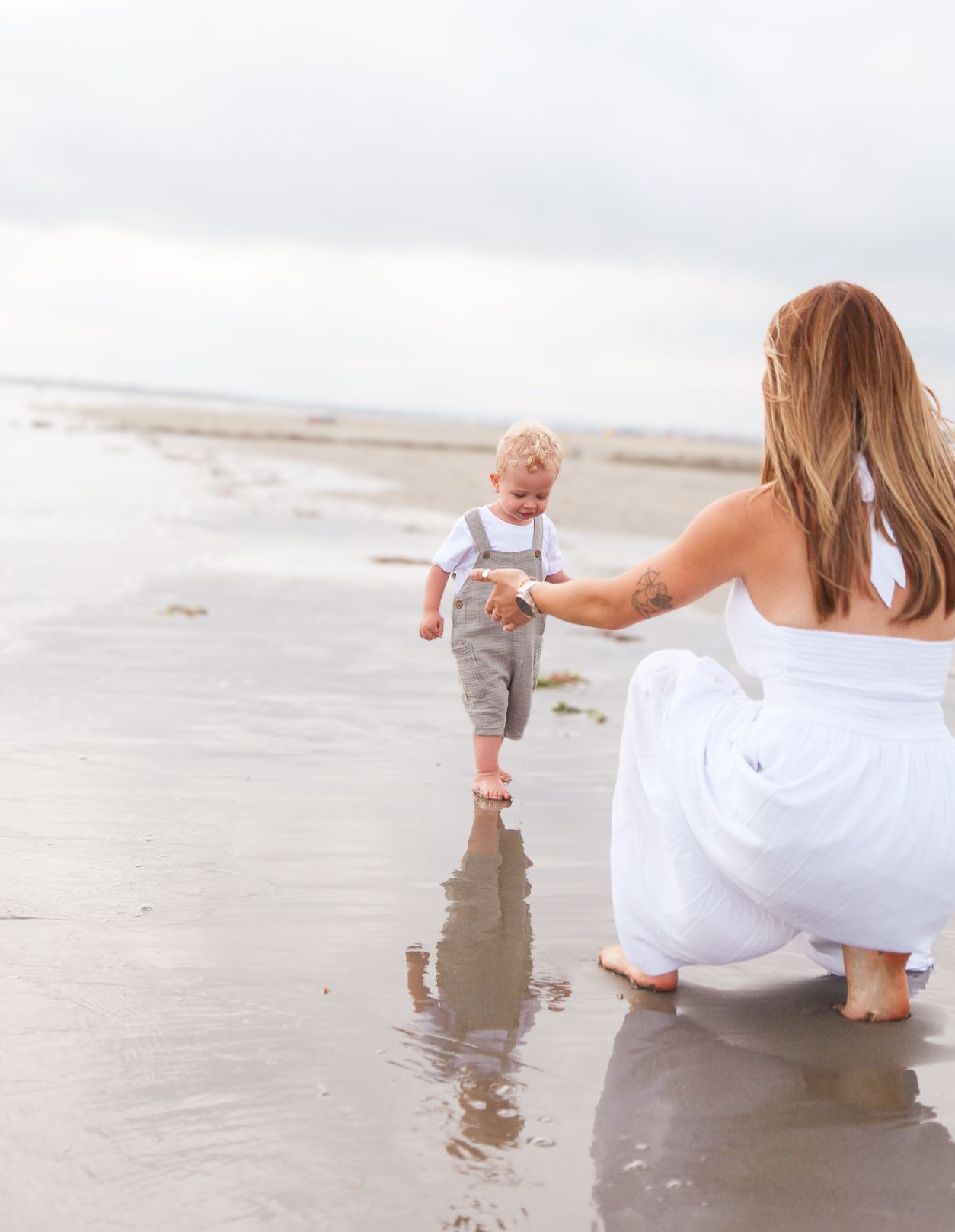 A mother and toddler playing together on a sandy beach at the water's edge.