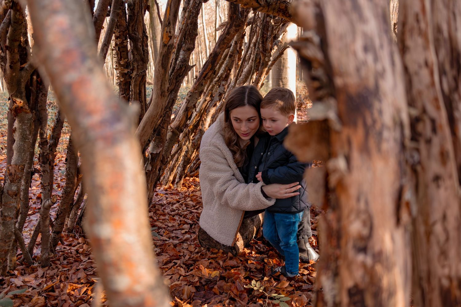 Family group poses between tree trunks in an autumn forest setting.