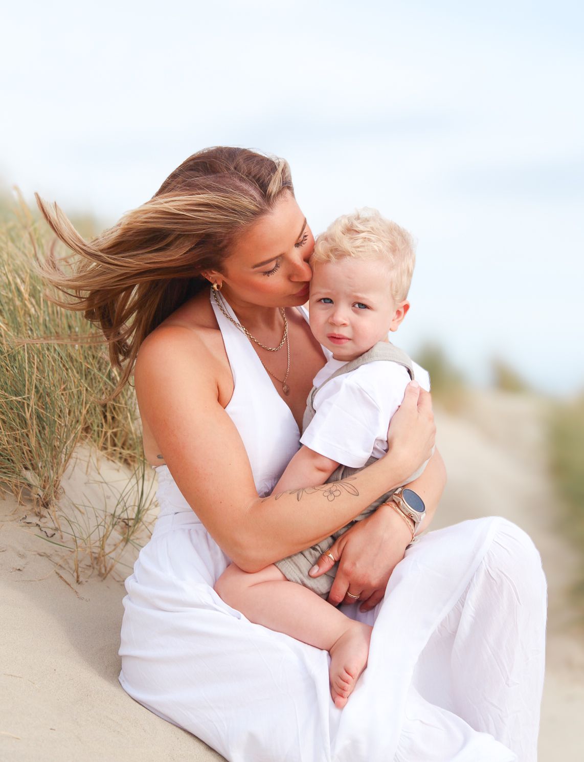 Intimate family moment captured between parent and child on sunny beach dunes.