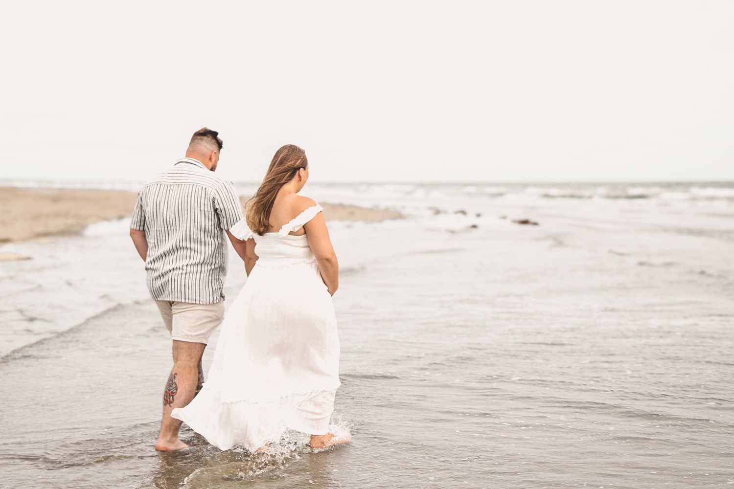 Couple walks hand in hand along peaceful beach shoreline at sunset.