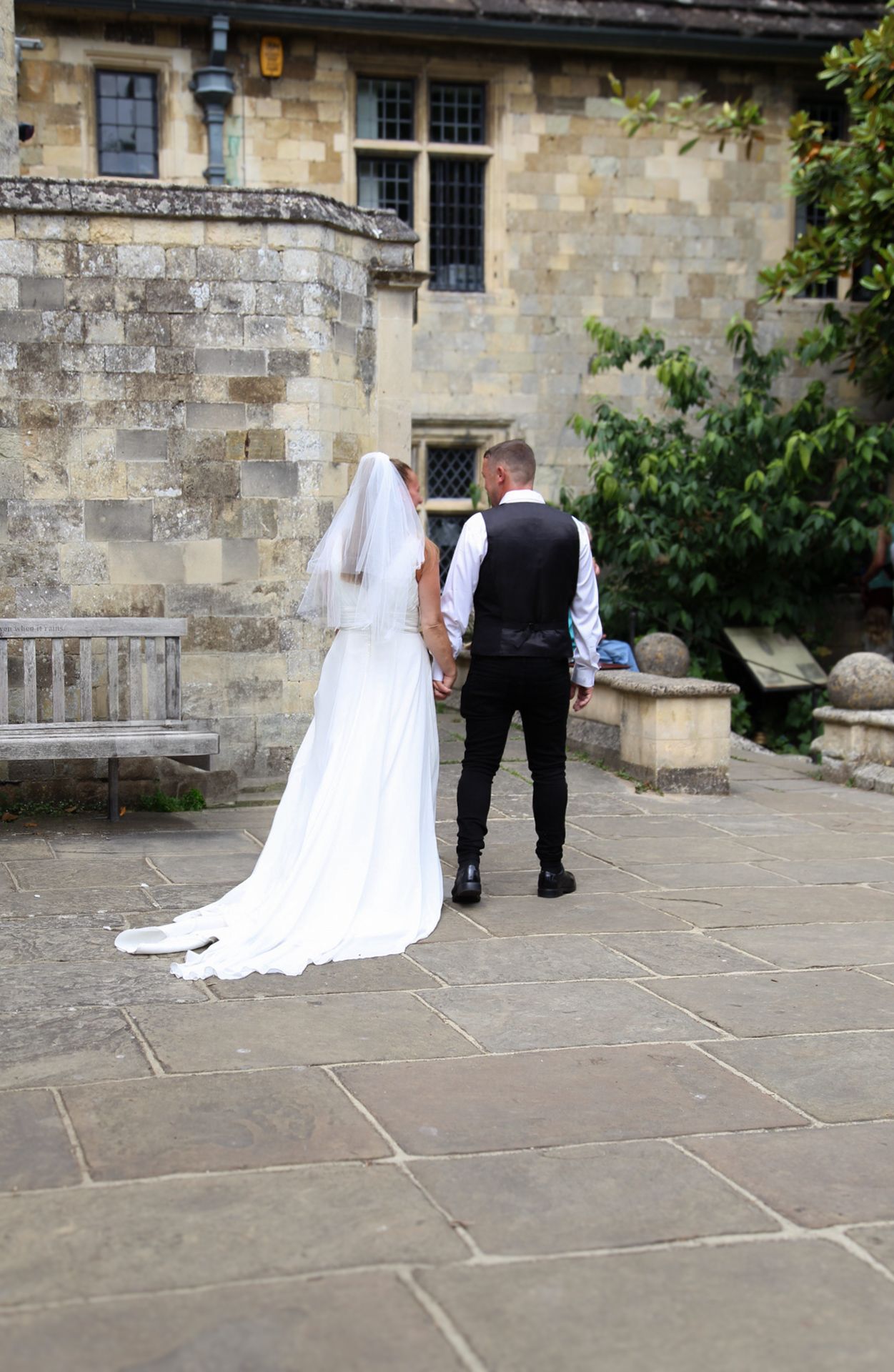 A wedding couple walks together on stone pavement outside a historic building.