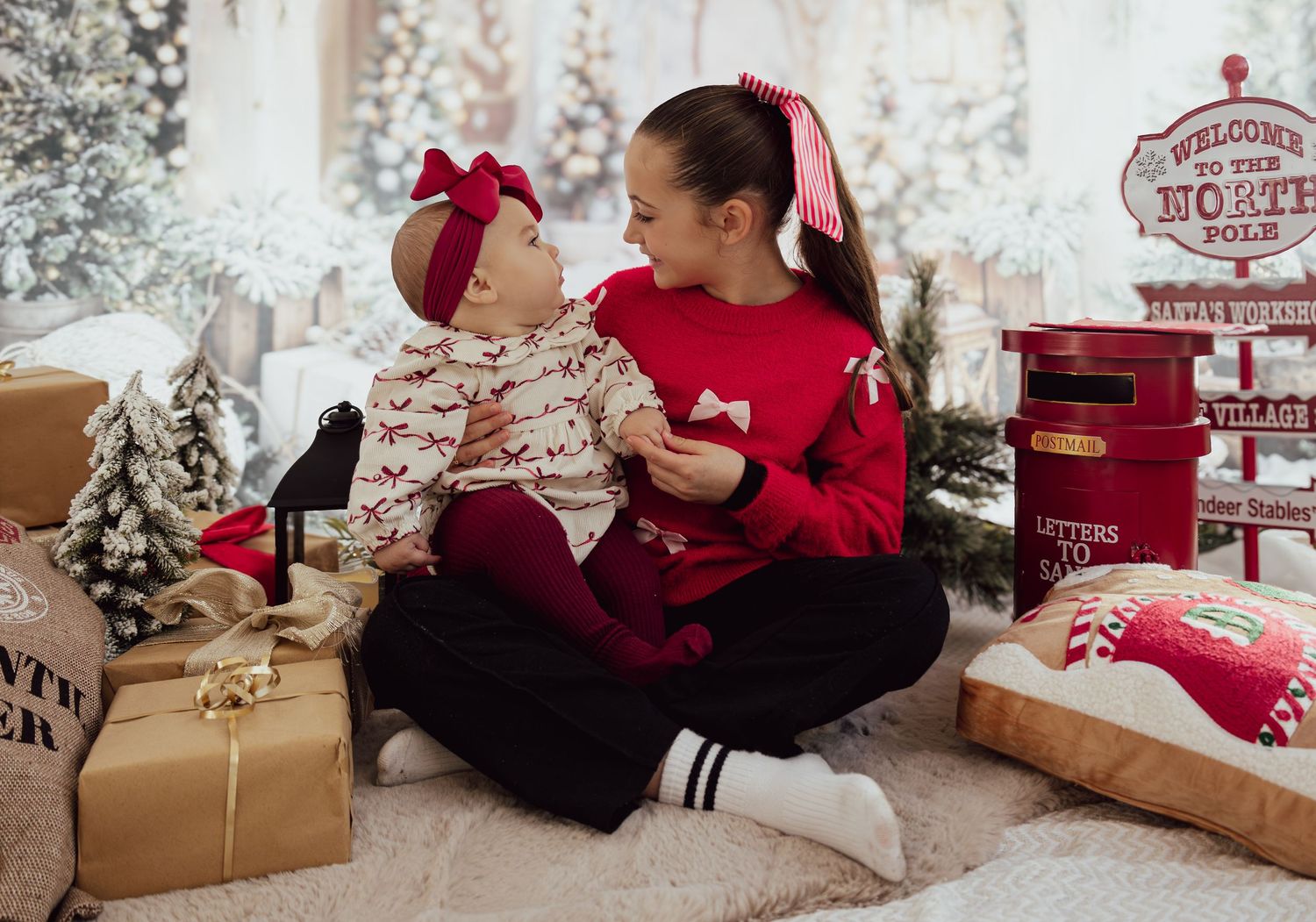 Two people in red holiday outfits sit among Christmas presents and decorations.