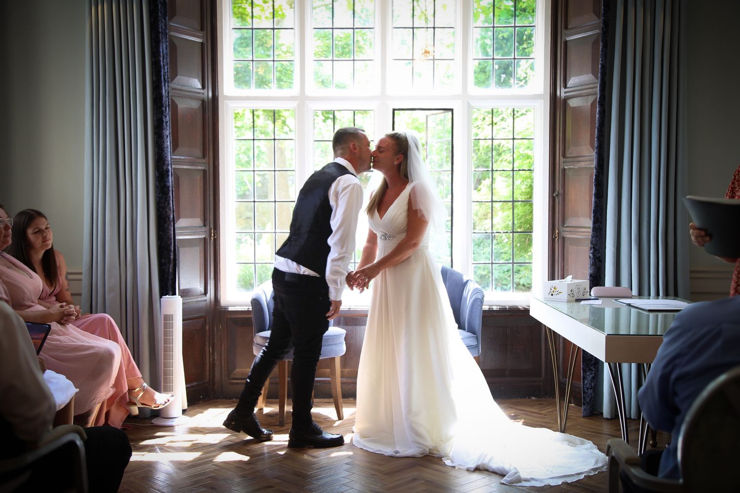 A romantic first dance moment captured in front of sunlit windows at an indoor wedding venue.