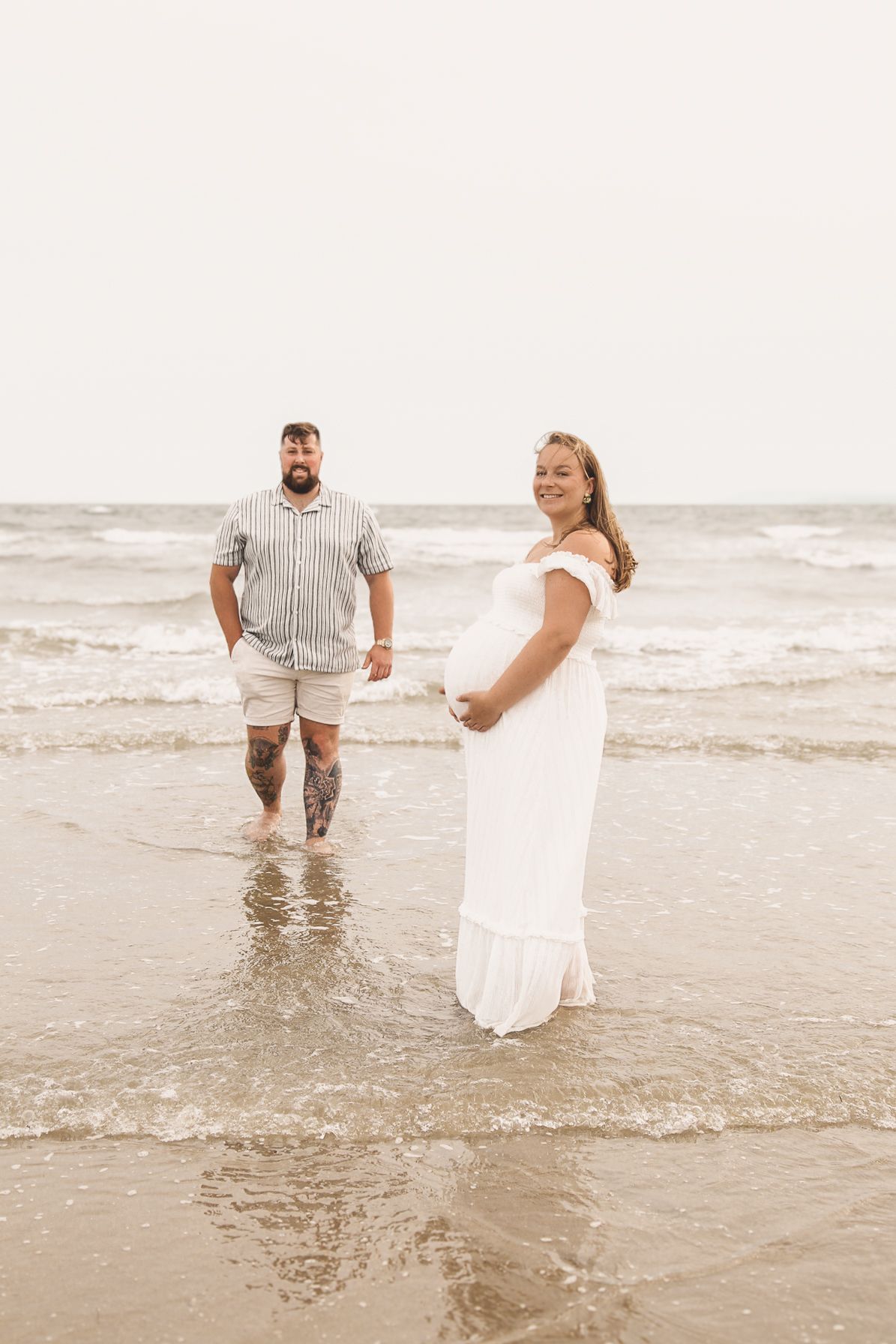 Two people splash and dance together in shallow ocean water at sunset.