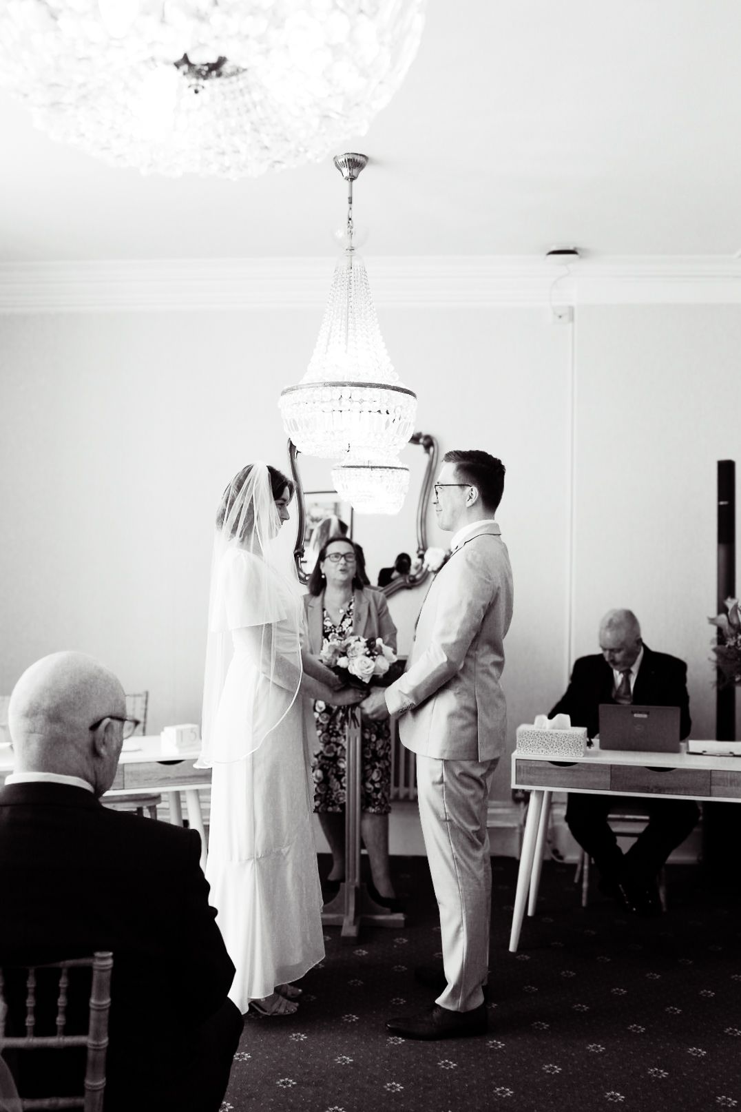 Black and white wedding ceremony photo under an elegant chandelier.